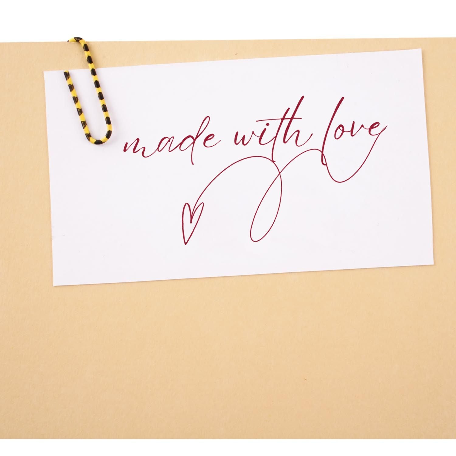 Burgundy made with love stamp on a white card, clipped with a yellow-and-black paper clip against a beige background.