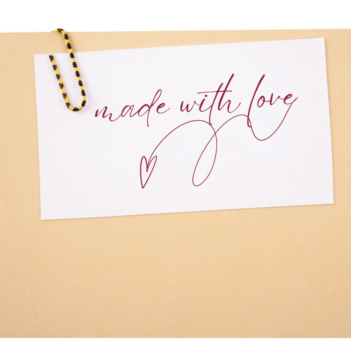 White card with burgundy made with love script, heart, and yellow-black paperclip on beige background, for stamp and seal products.