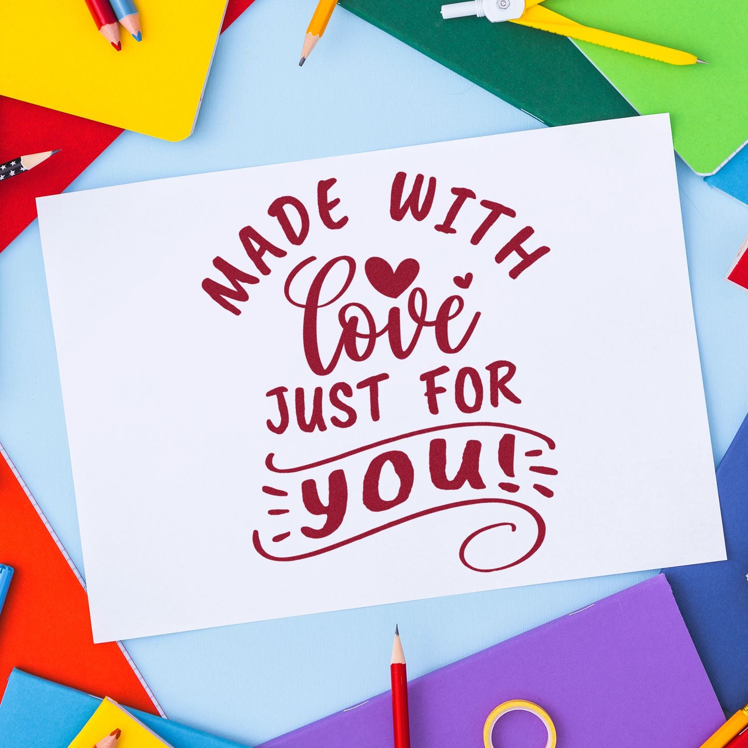 Burgundy love stamp reading Made with love just for you on white card, framed by colorful pencils and notebooks.