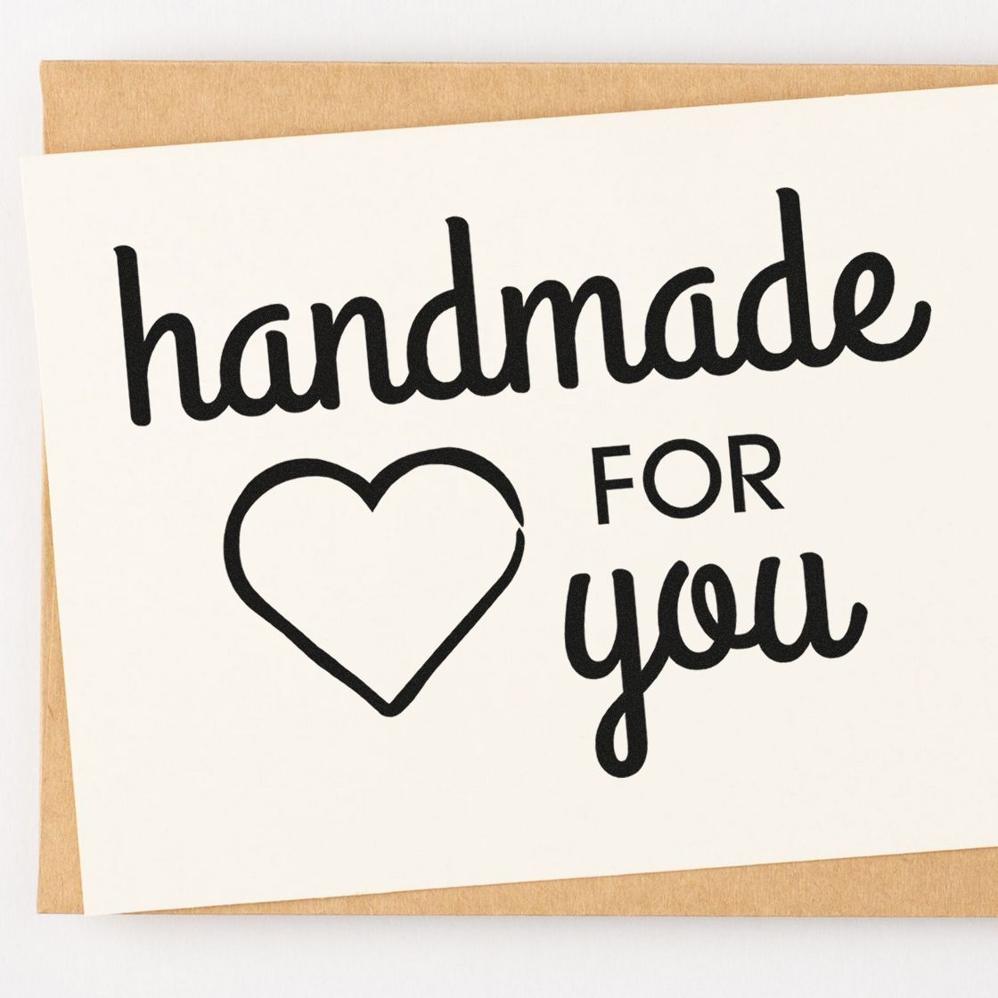 Black handmade for you stamp design with heart seal on white card over kraft paper background.