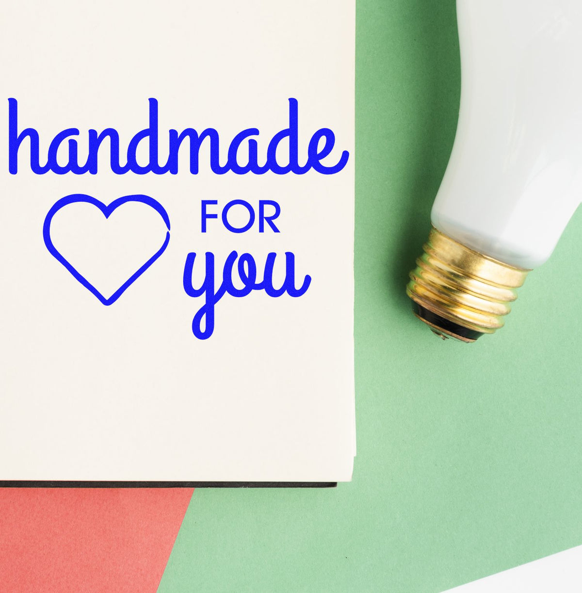 Blue handmade for you stamp with heart on white card, beside a white-and-gold sealing tool on green paper.