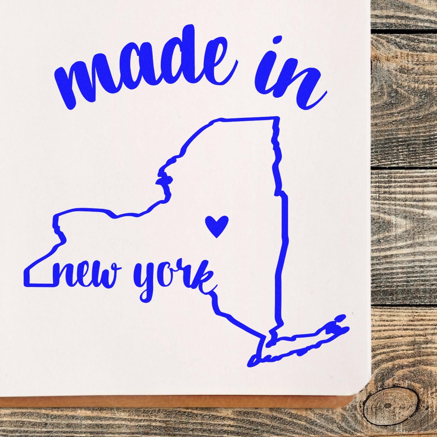 Made in New York Stamp Pre-Inked featuring a blue outline of New York state with 'made in new york' text and heart symbol on a wooden surface.