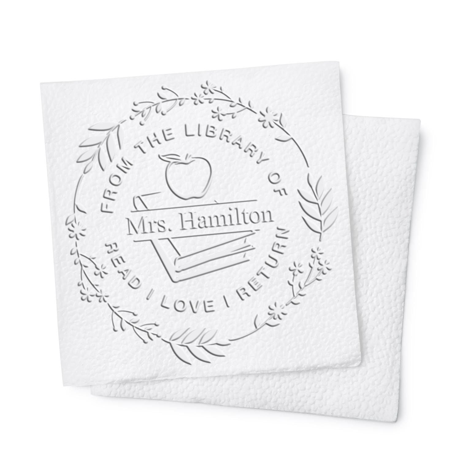 White embossed library return stamp seal with floral wreath, apple, books, and Mrs. Hamilton text.