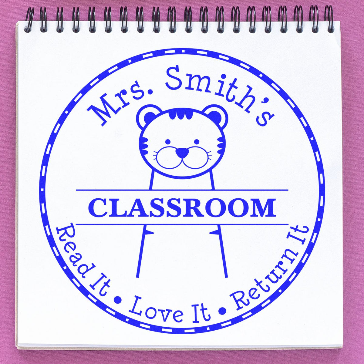 Blue classroom stamp seal with bear mascot, Mrs. Smiths Classroom and Read It Love It Return It on white, pink background