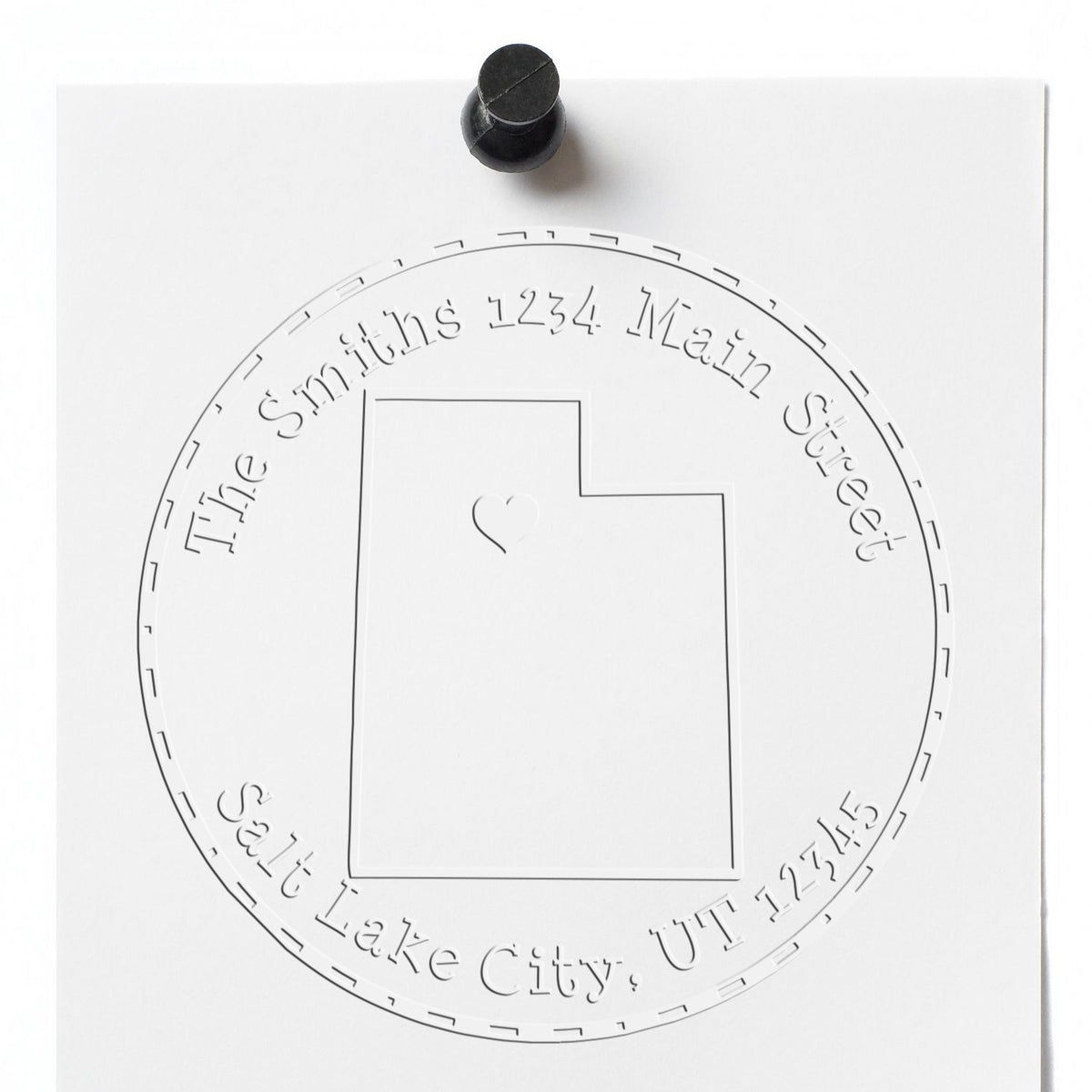 White embossed custom seal stamp on paper with black stamper, circular text, Utah outline, and heart center.