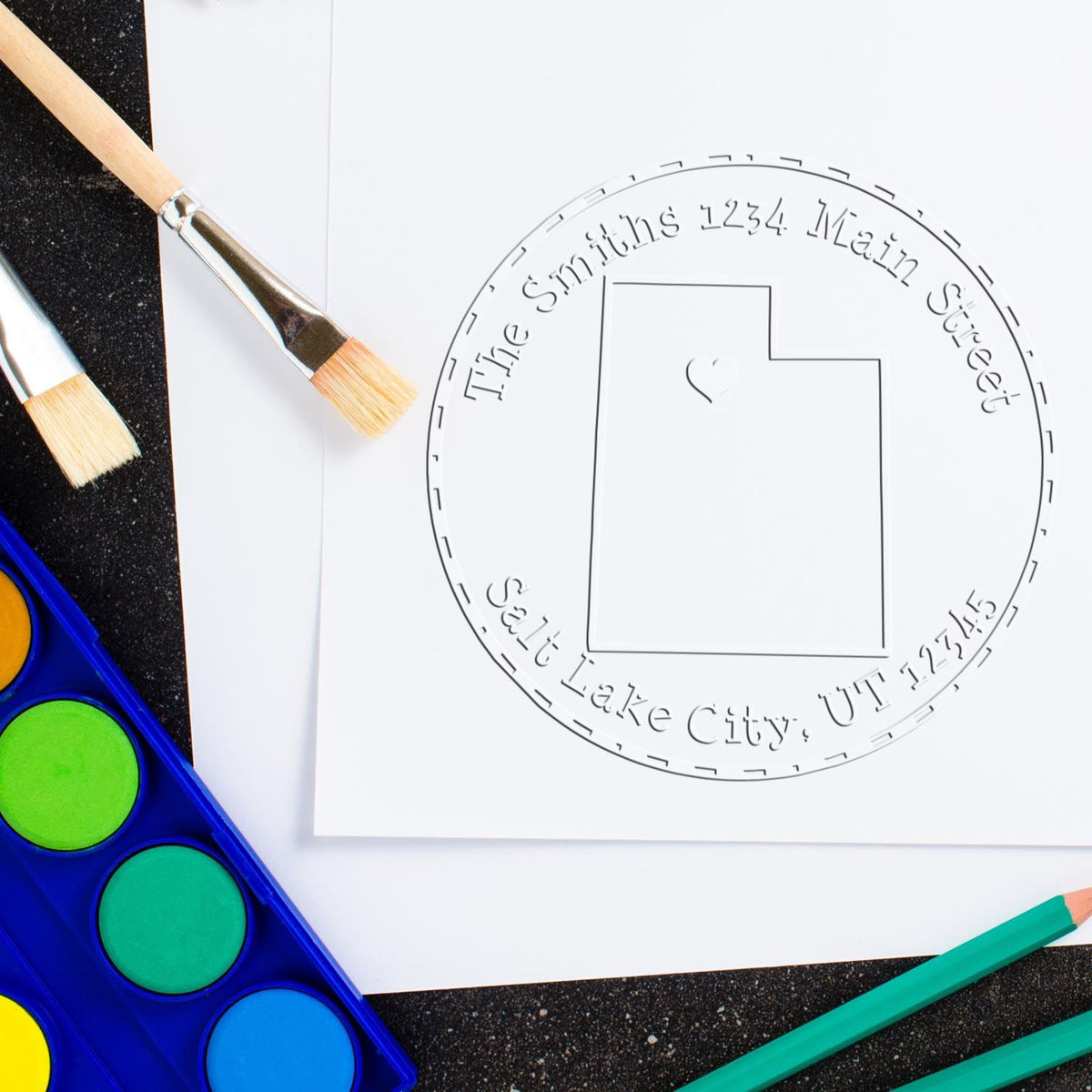 Custom stamp and seal design on white paper with gray circular outline, paintbrushes, and colorful art supplies.