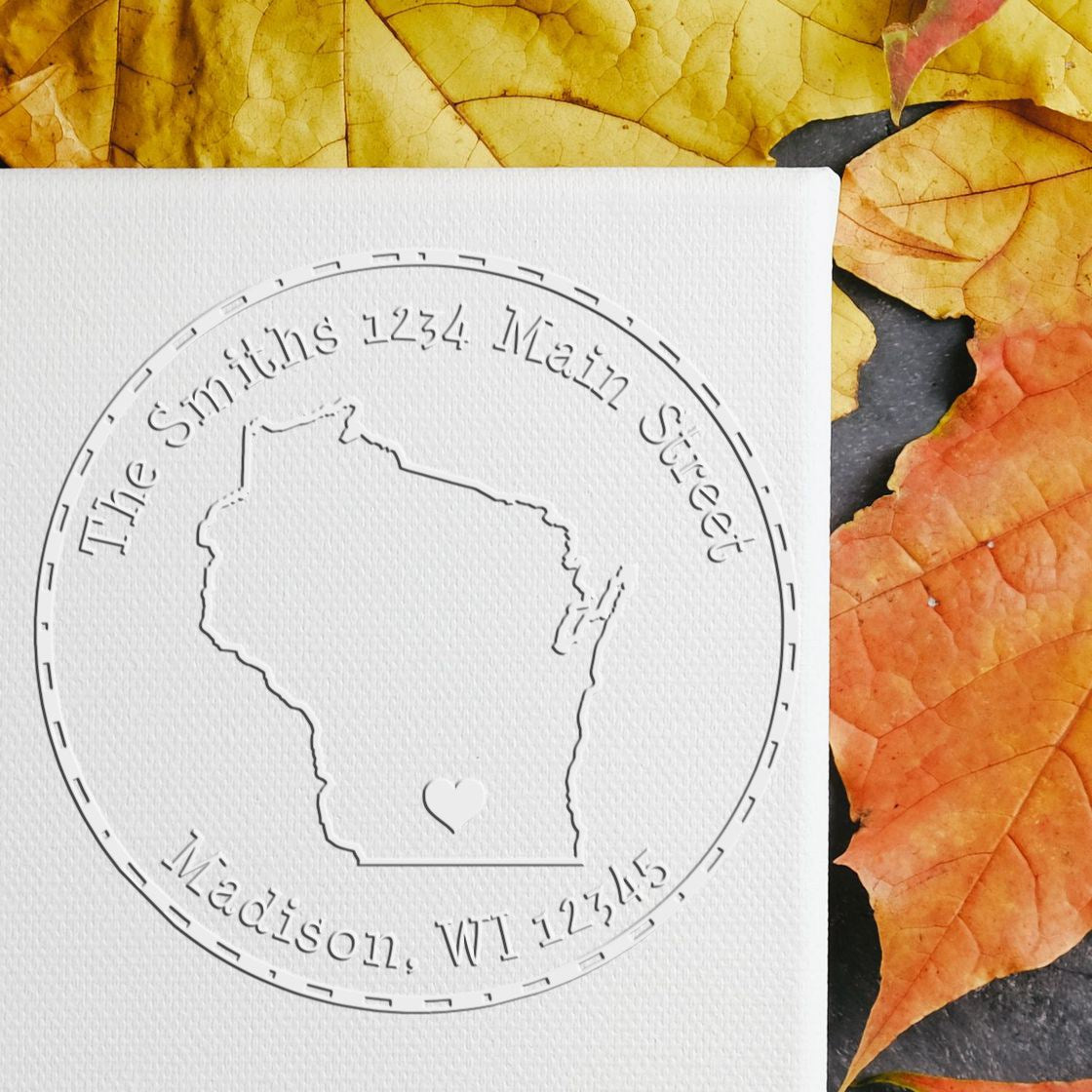 Embossed circular stamp seal on white textured card, featuring Wisconsin outline, Madison address, and yellow-orange autumn leaves.