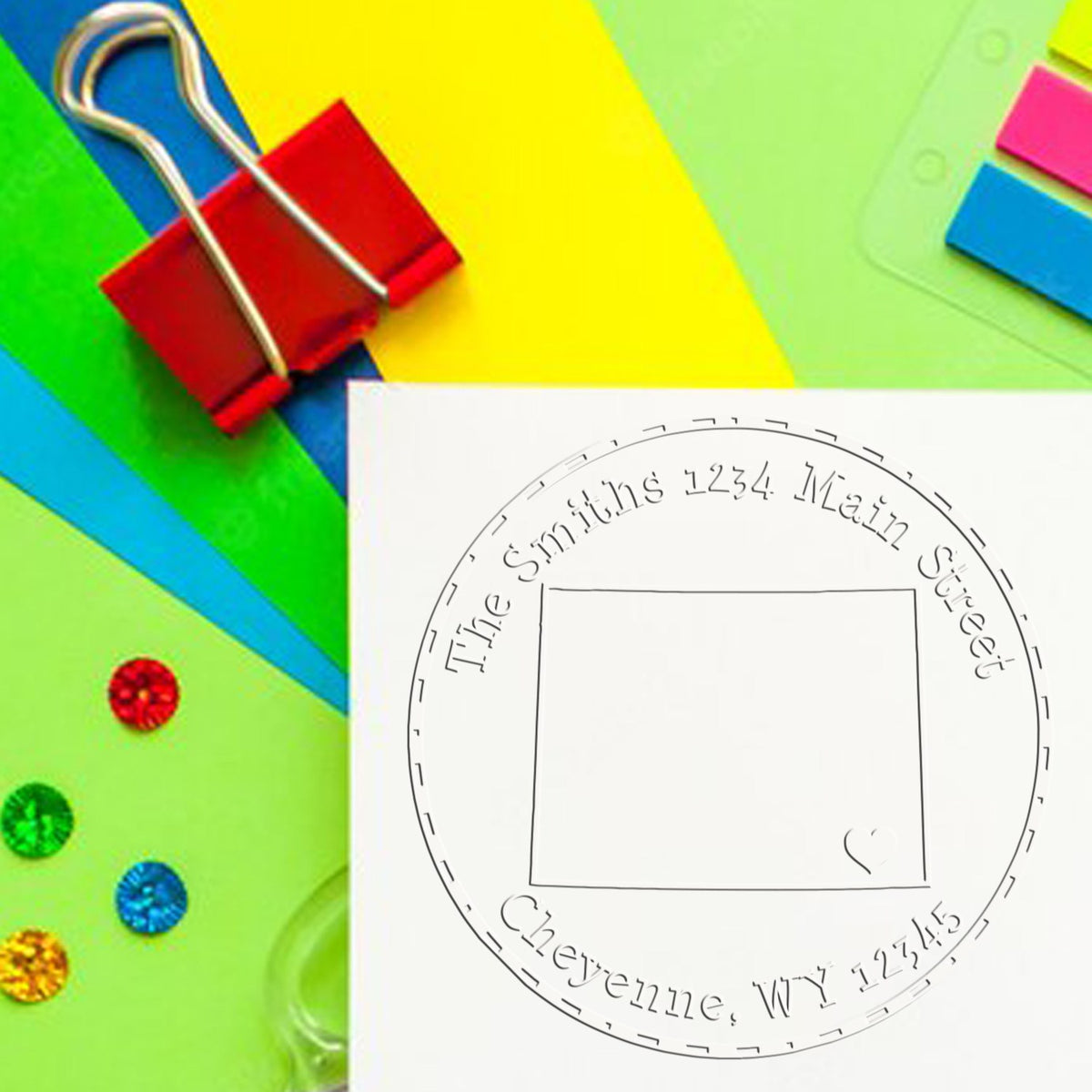 Custom round stamp seal on white paper with red binder clip and bright green, yellow, blue, and pink office supplies.