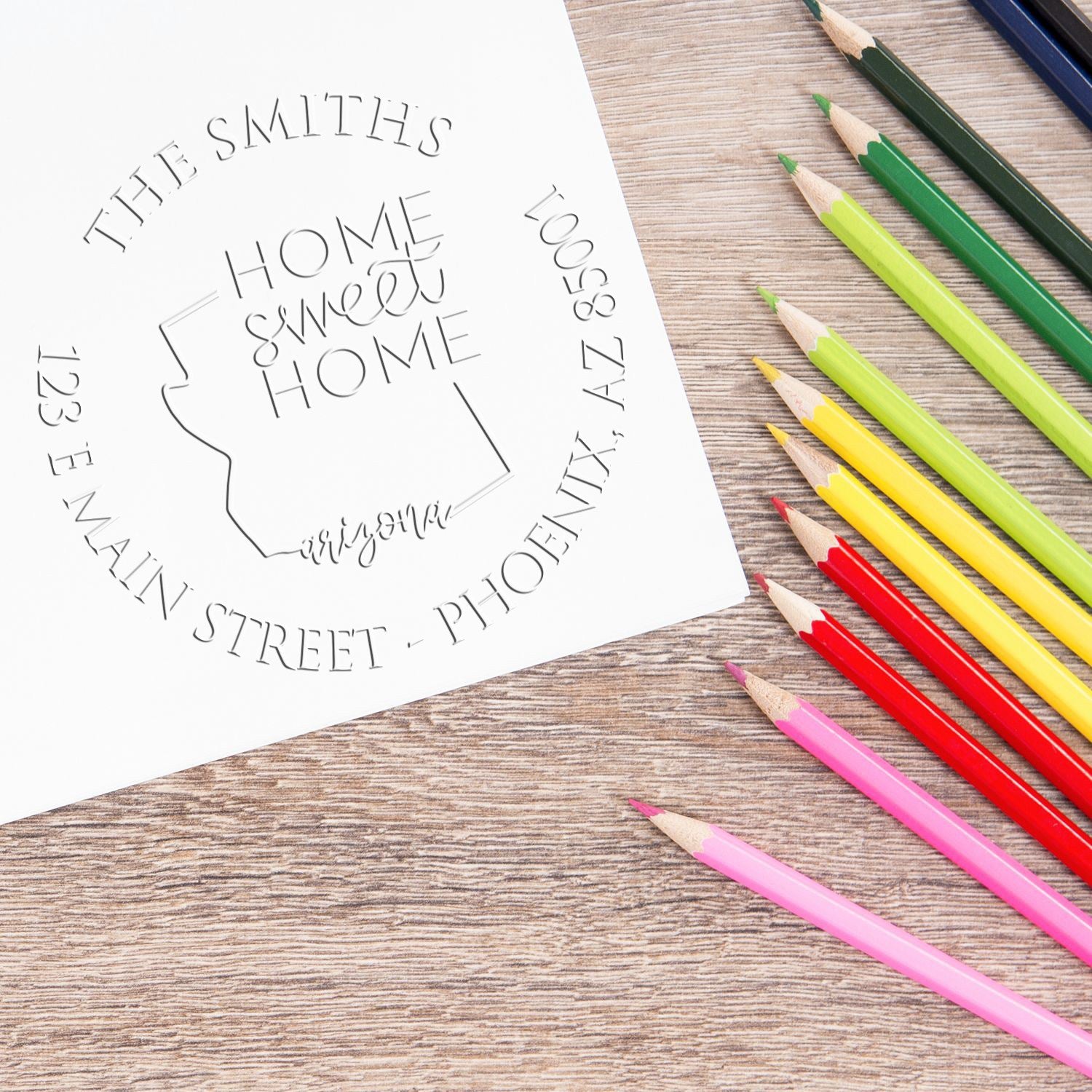 Custom home stamp and seal for The Smiths, embossed on white paper, beside bright green, yellow, red, and pink pencils.