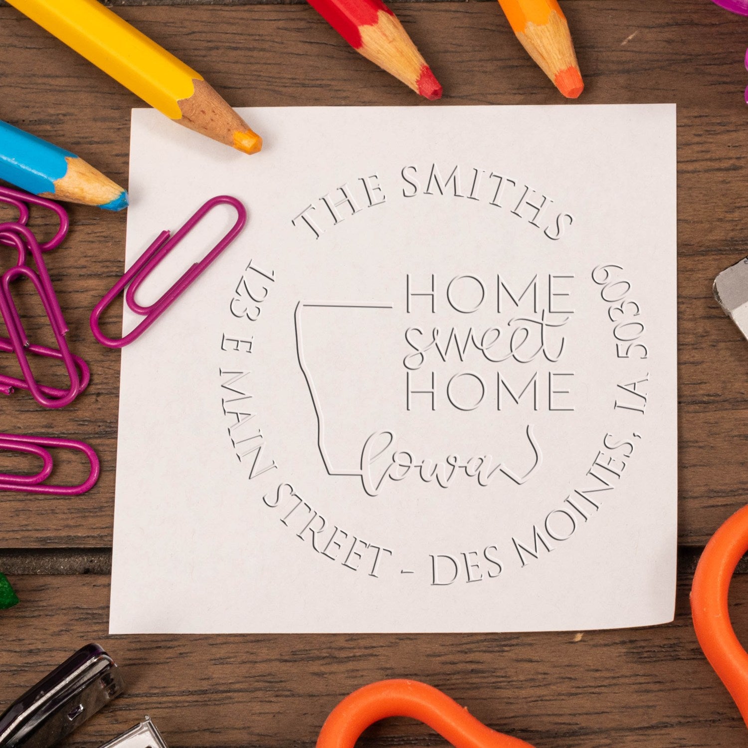 Embossed white stamp seal with House Sweet Home, The Smiths, and Iowa, framed by colorful crayons and pink paper clips.