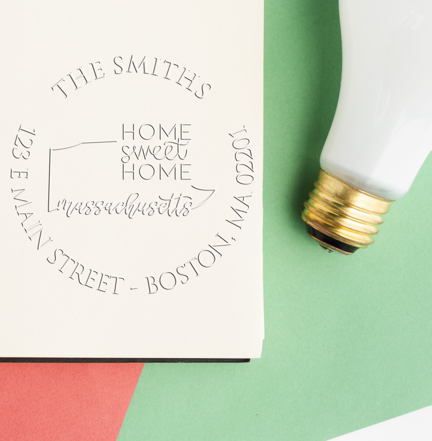 Embossed stamp and seal on white paper beside a white-and-gold embossing tool over green and red background