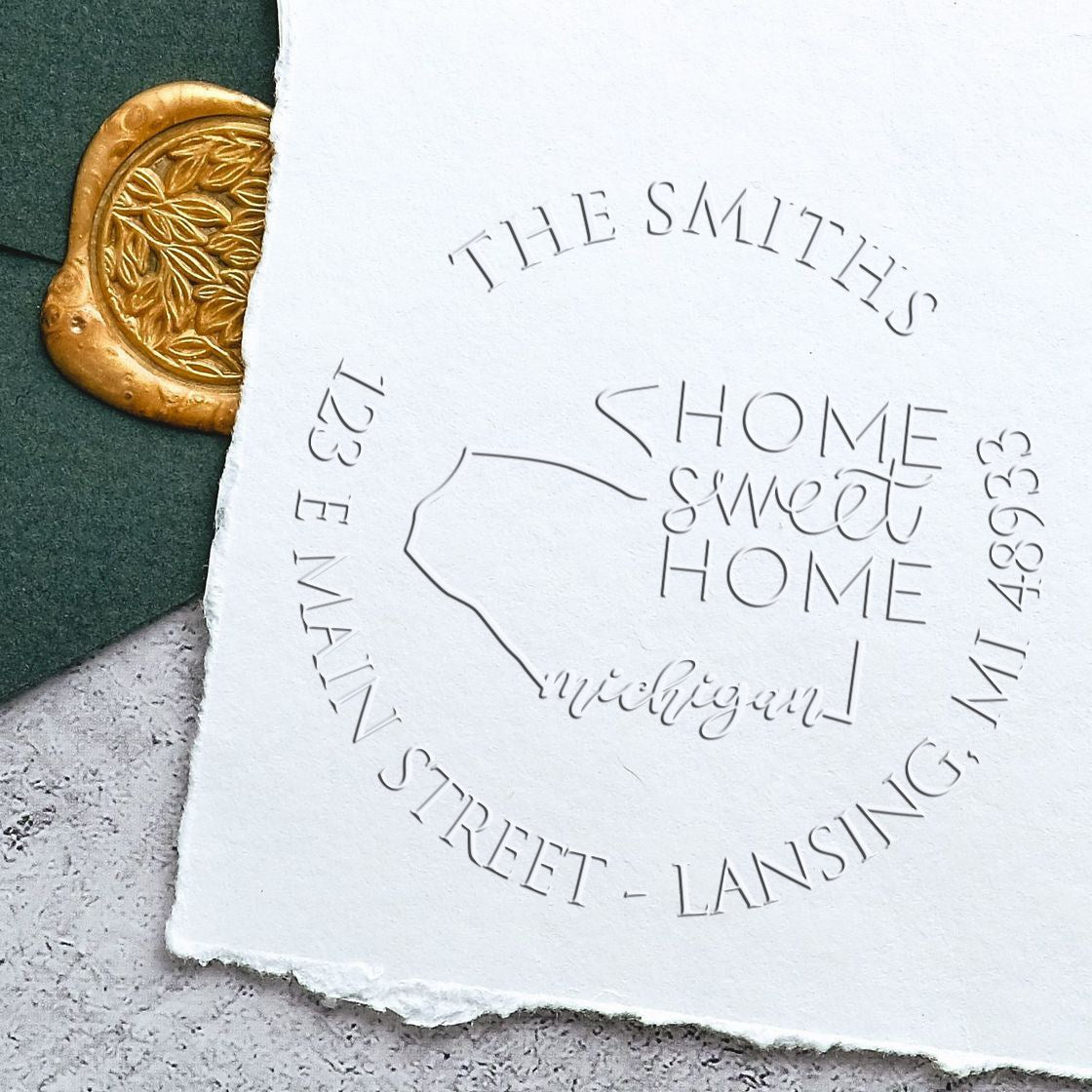Embossed white paper stamp seal with Home Sweet Home Michigan design, beside a gold wax seal on dark green background.