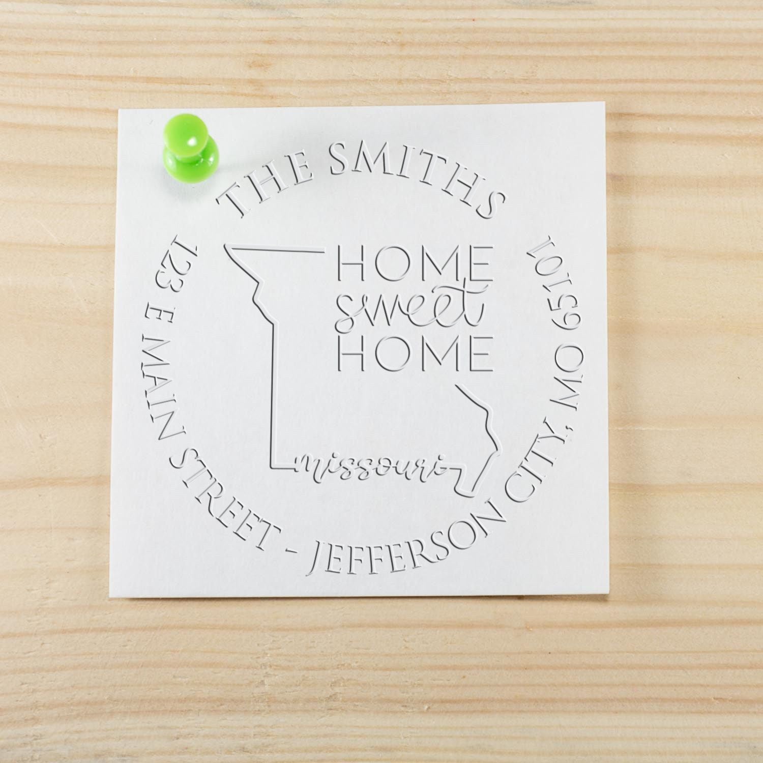 Custom white embossed stamp seal with Missouri outline and Home Sweet Home, accented by a green pushpin on a wood background.