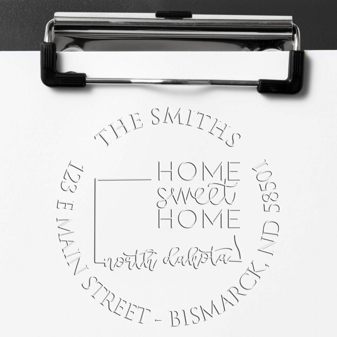 Chrome clipboard displaying a white sheet with an embossed custom seal stamp, gray text reading Home Sweet Home and The Smiths.