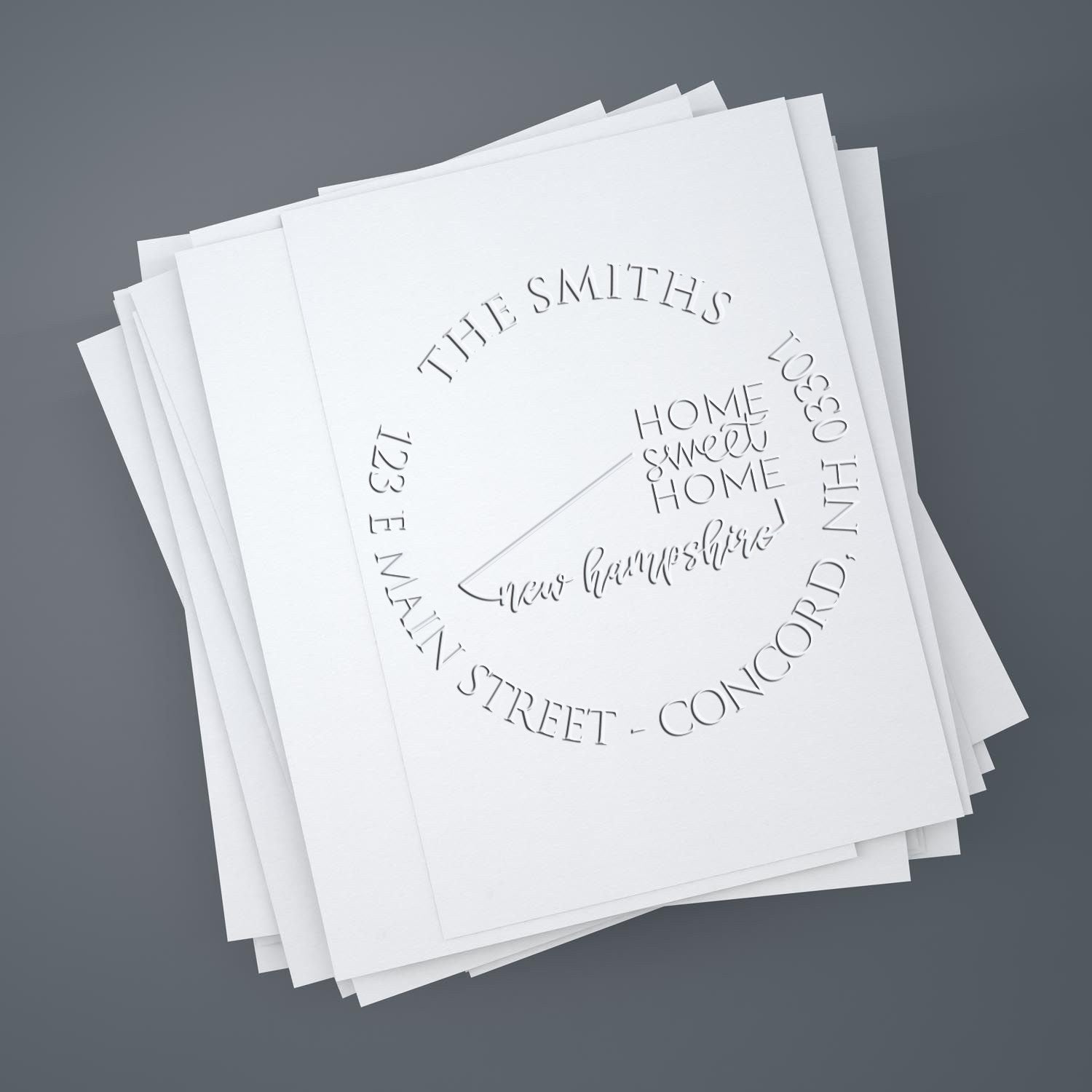 Embossed white stamp and seal samples on stacked paper sheets, with circular text and a home logo on a gray background.