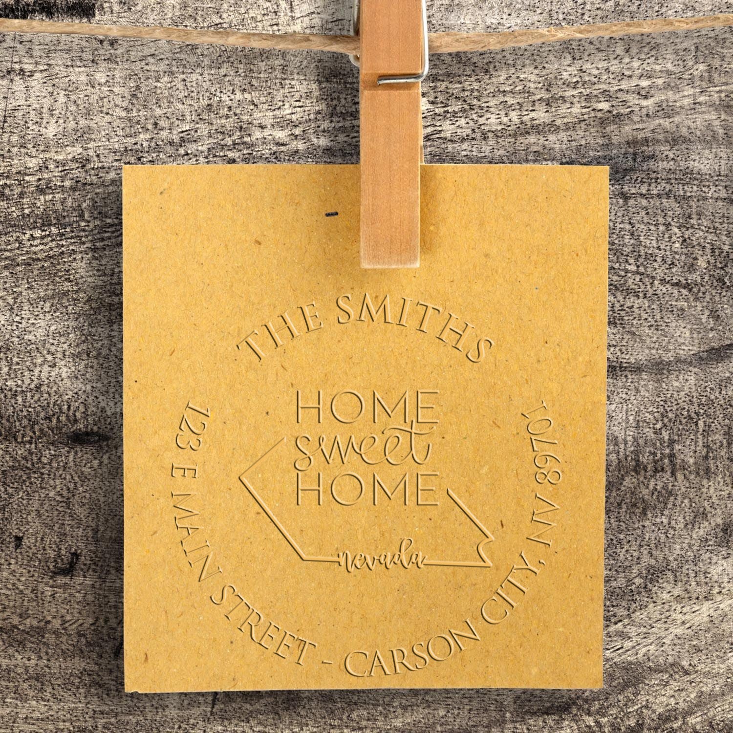 Tan embossed custom stamp and seal with house outline and Home Sweet Home, clipped against a gray wood background.