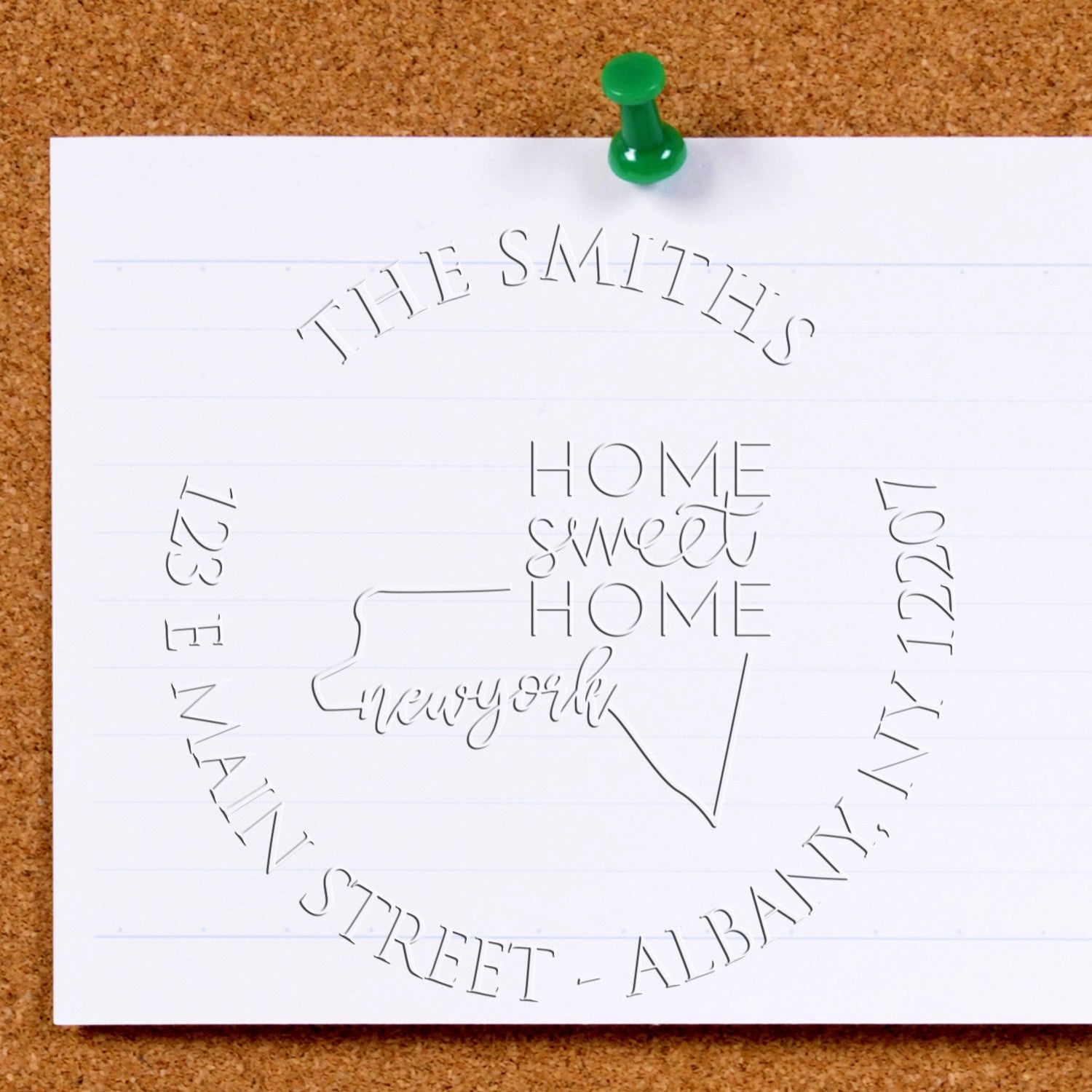 Green pushpin on white paper showing embossed stamp and seal design for “The Smiths” home sweet home, New York.