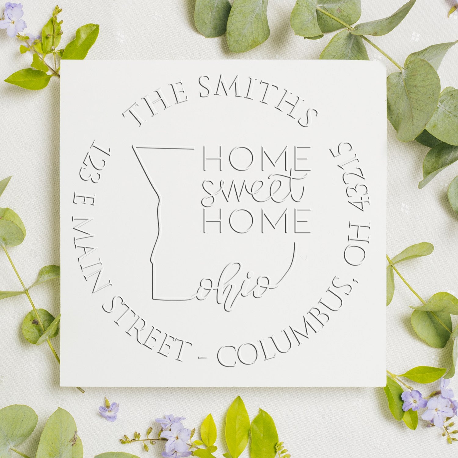 White custom embossing seal stamp with Ohio outline and Home sweet home text, framed by green leaves and purple flowers.