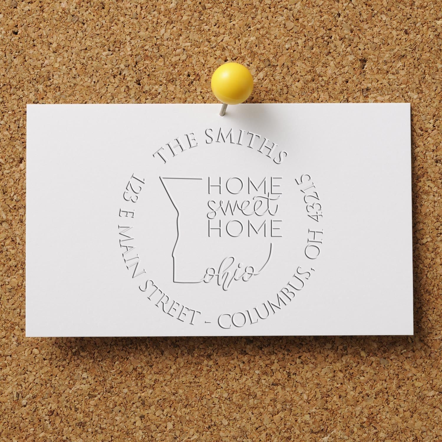 White embossed custom stamp and seal on corkboard, pinned with a yellow tack, featuring Home Sweet Home Ohio.