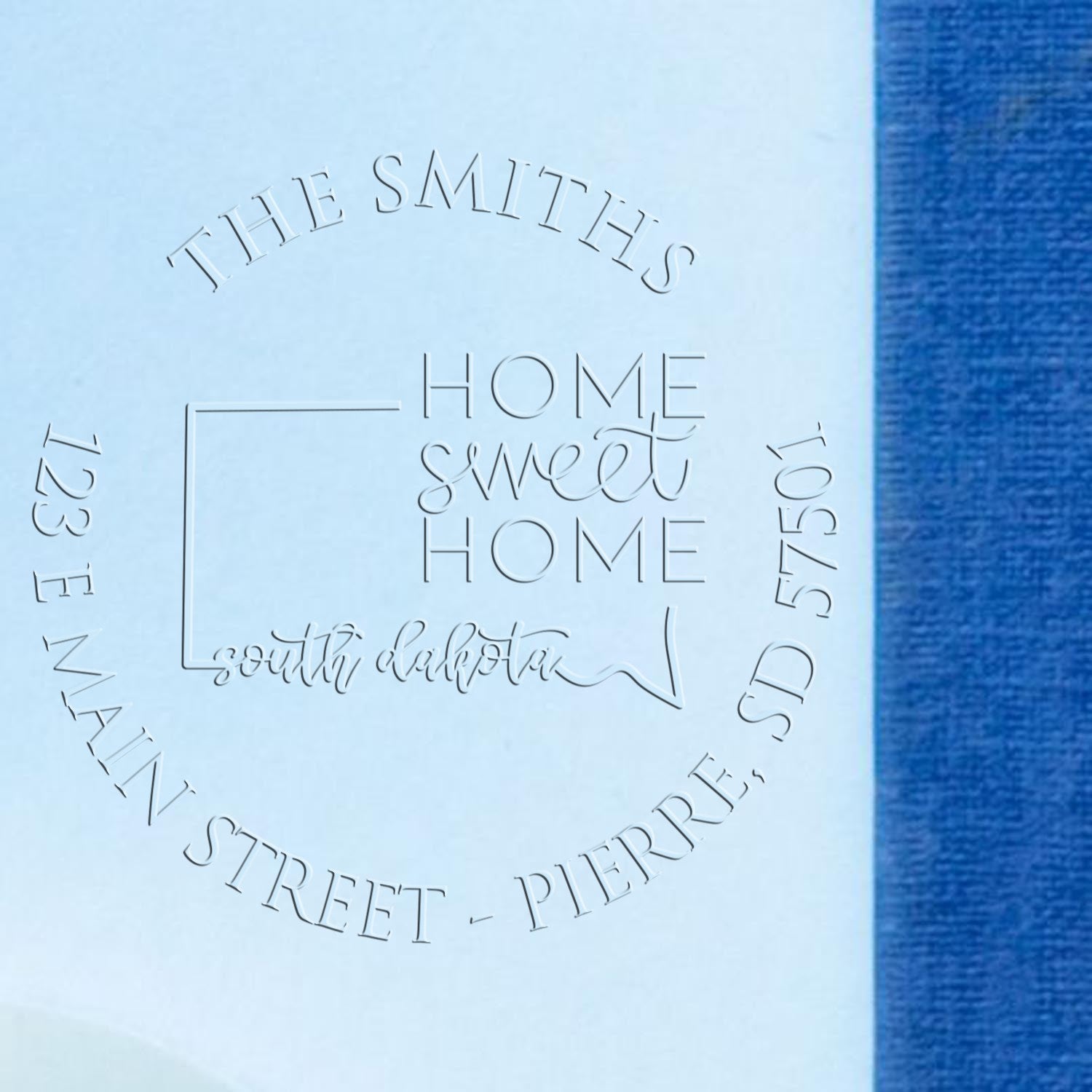 Custom embossing seal for The Smiths Home Sweet Home, raised silver-gray stamp on light blue paper with blue background.