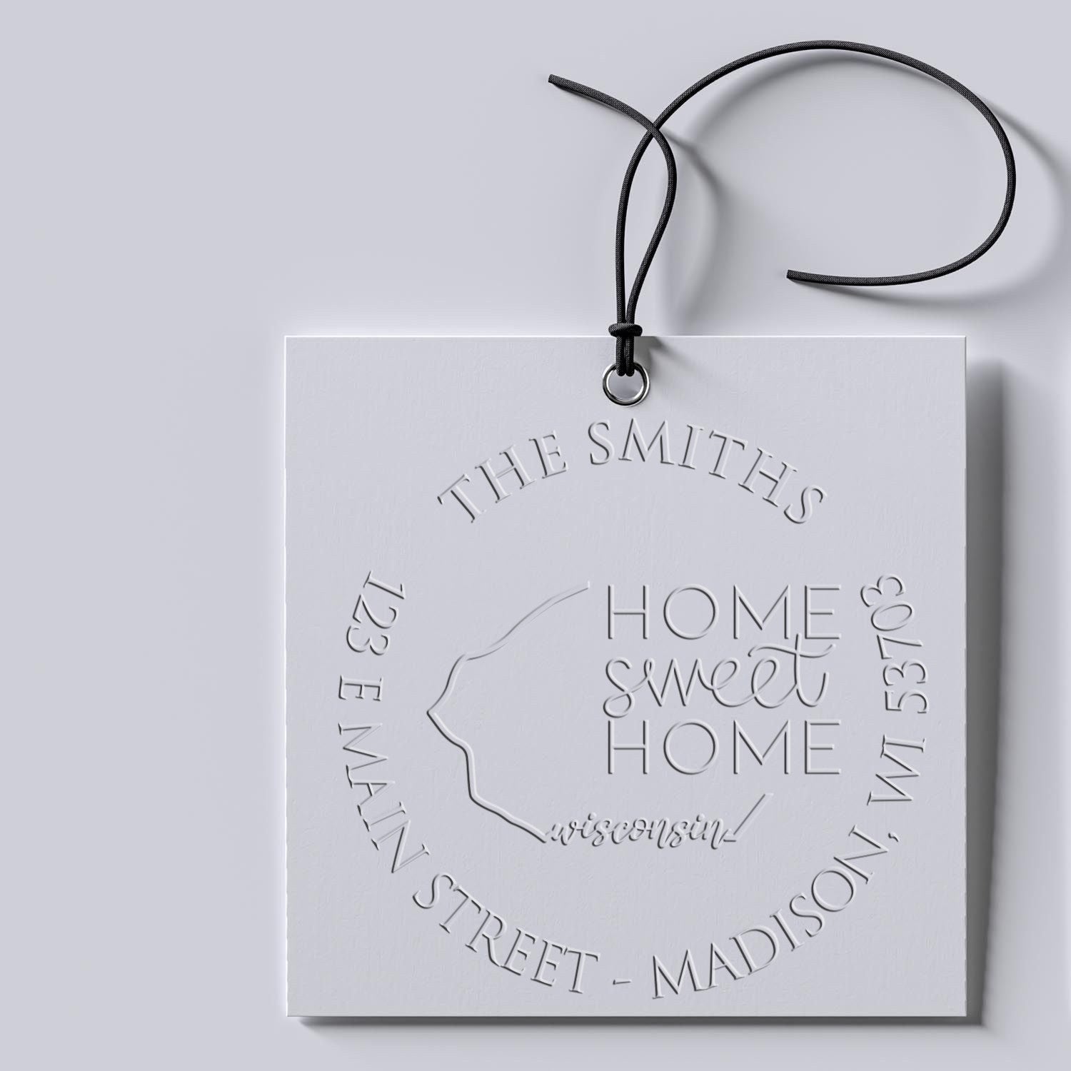 White embossed custom housewarming stamp and seal card with black cord on a light gray background.