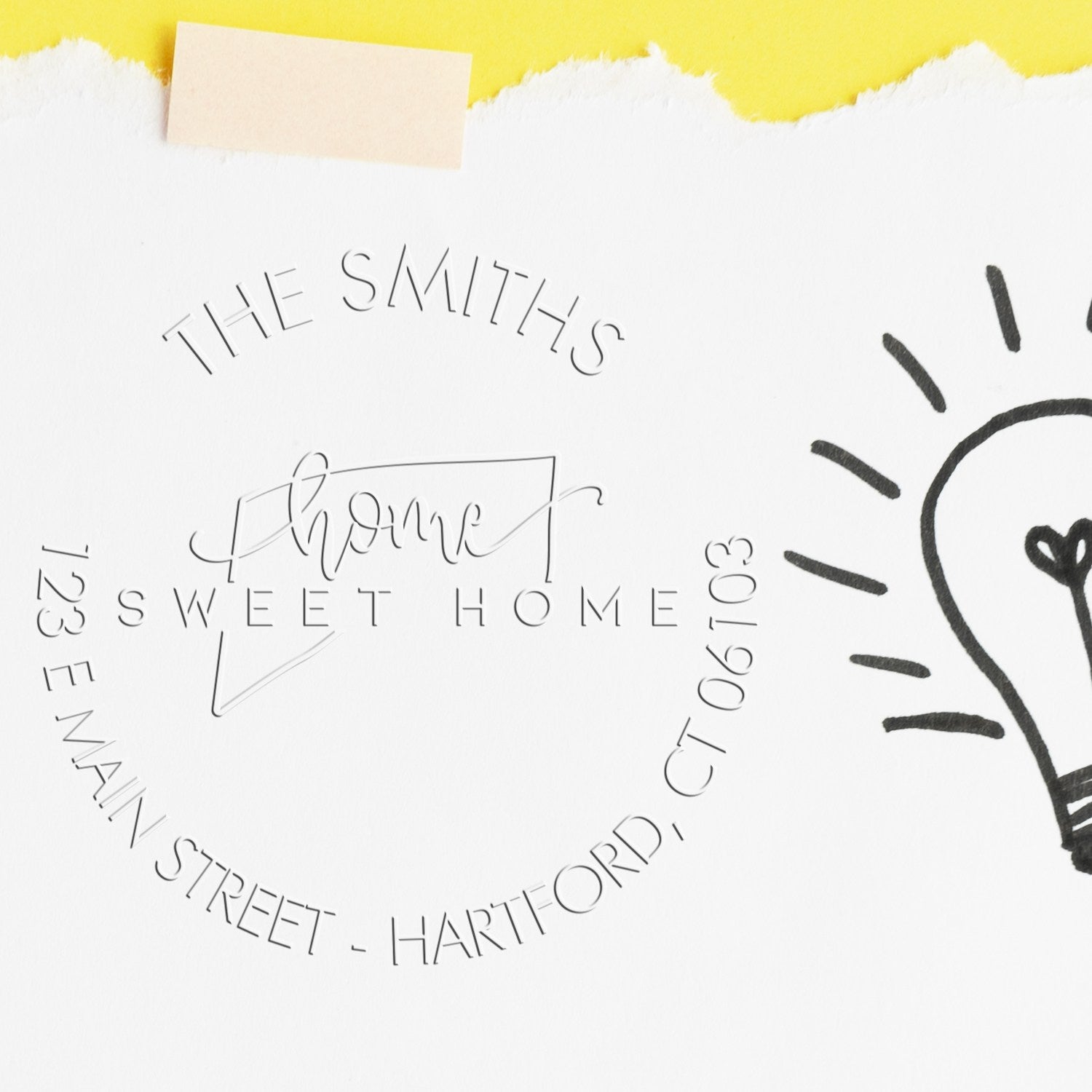Custom embossed stamp seal on white paper with black text, yellow tape, and a hand-drawn lightbulb accent.