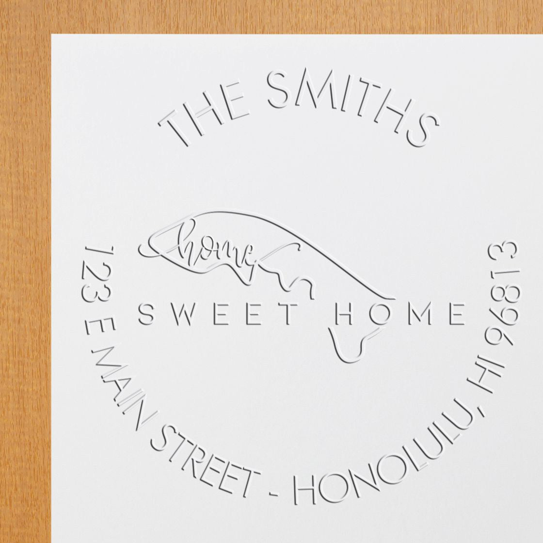 White embossed custom stamp seal for The Smiths, with Sweet Home, address text, and hand outline on white paper over wood.