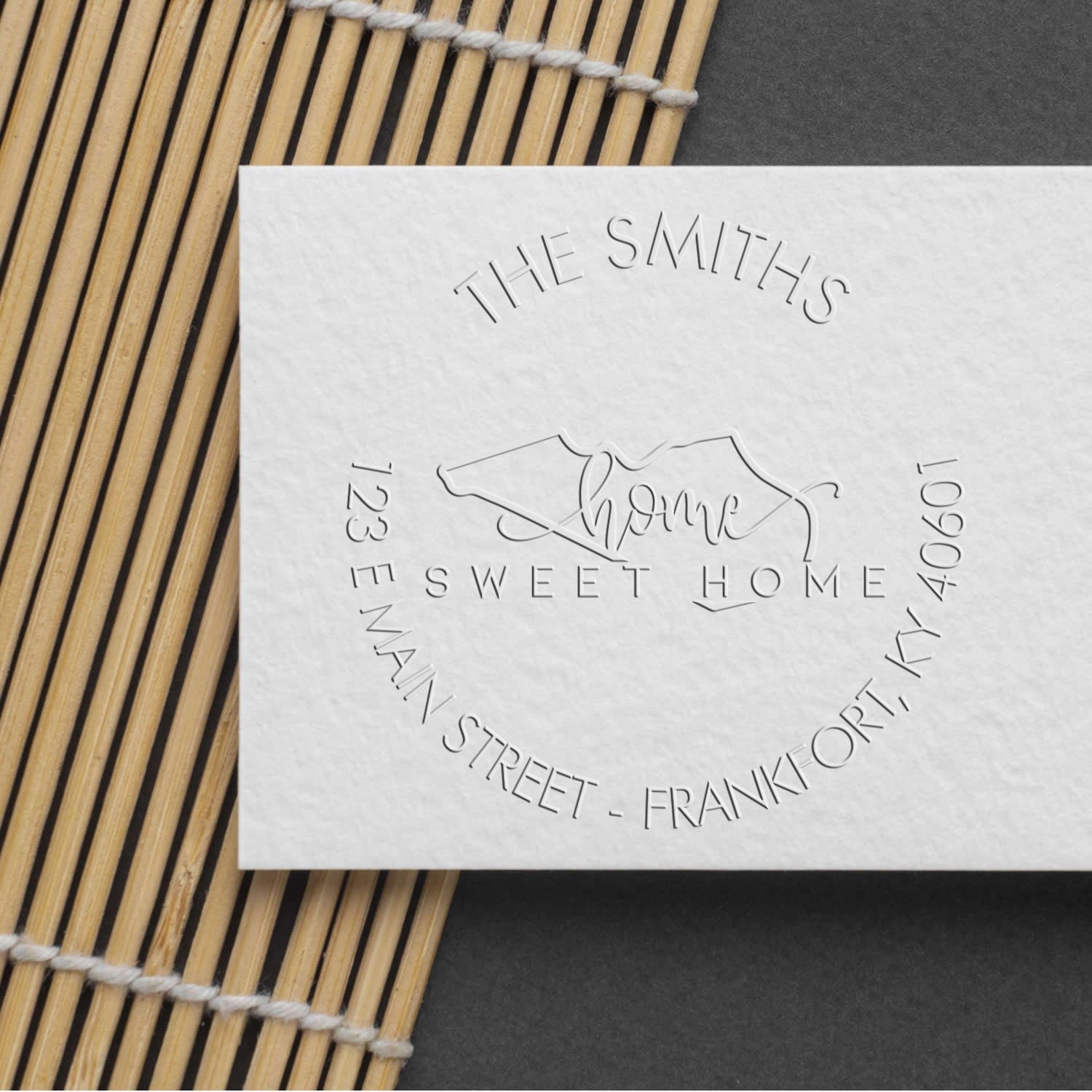 White embossed stamp and seal for The Smiths Sweet Home with silver-gray lettering on a bamboo mat.