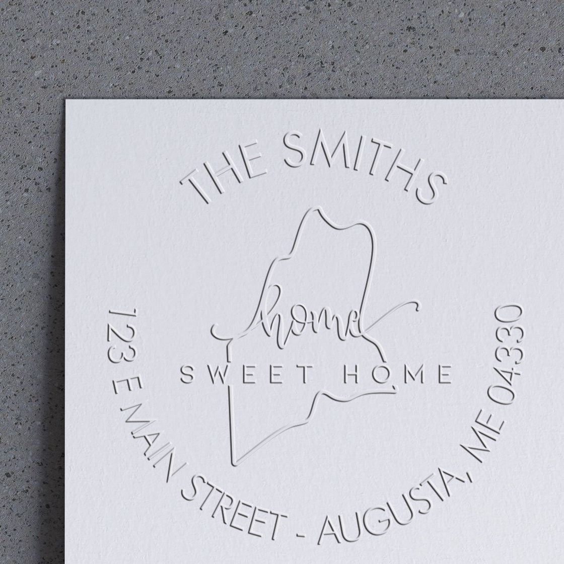 White embossed custom stamp seal with The Smiths, Home Sweet Home, and Maine outline on textured paper.