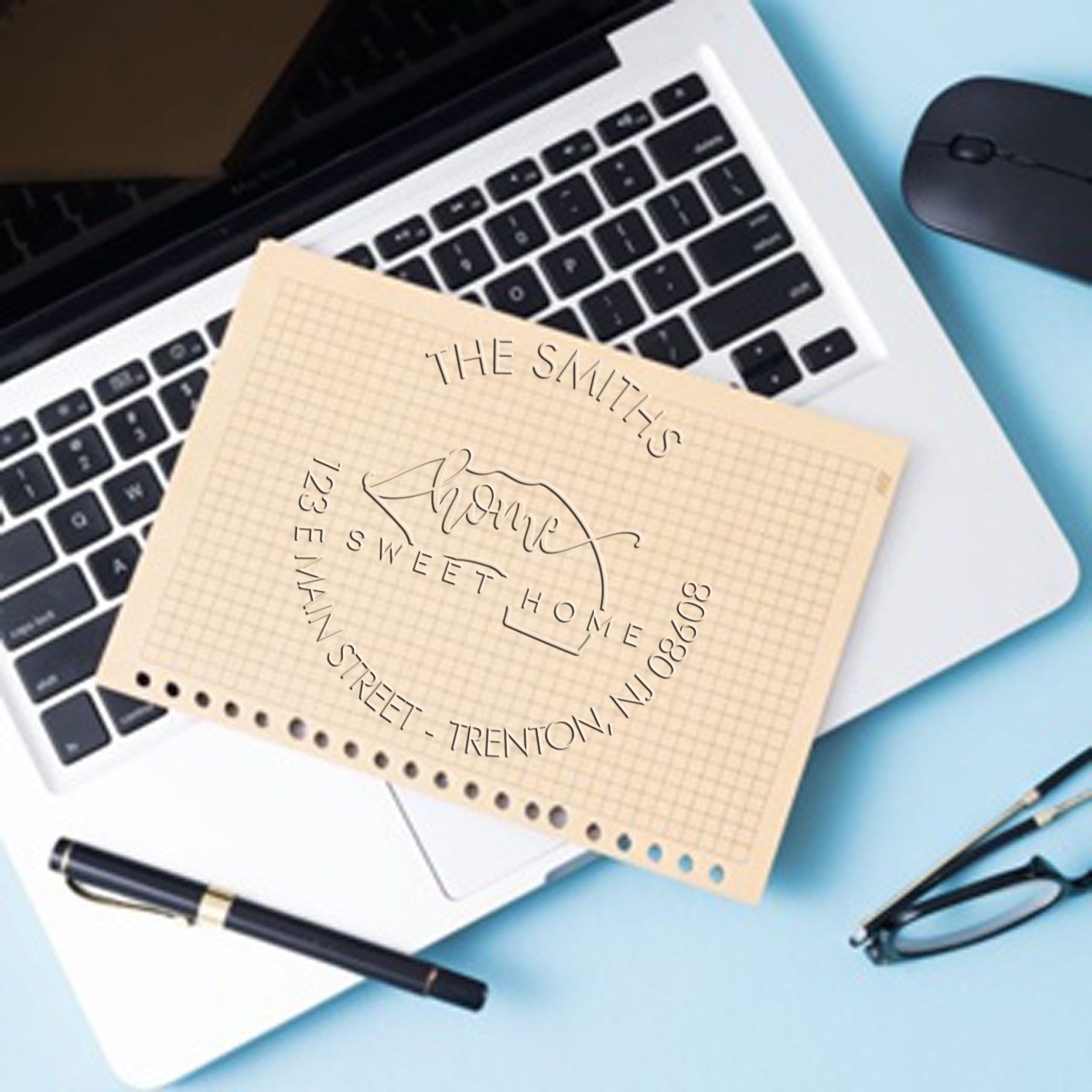 Beige custom home address stamp and seal on a laptop, with black pen, mouse, and glasses on a light blue desk.