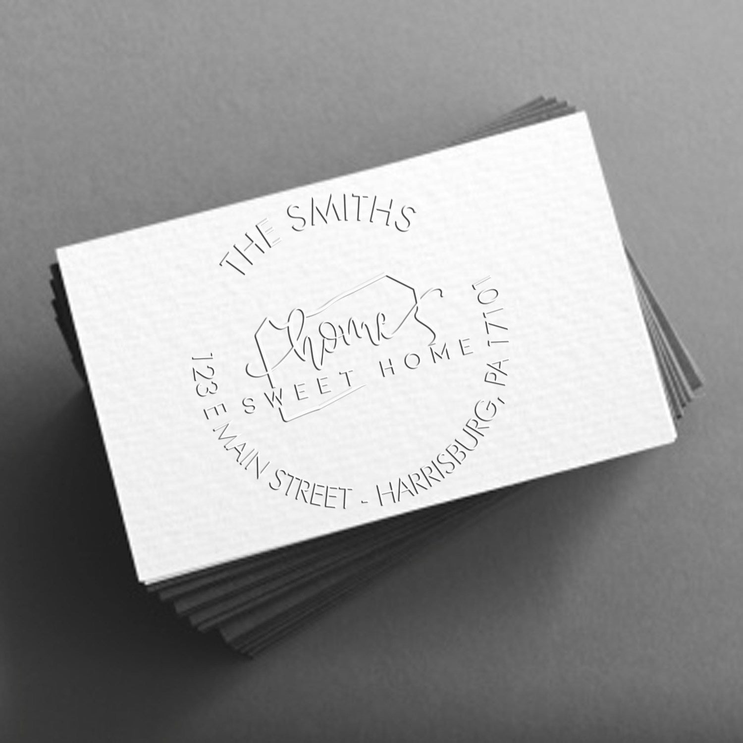 Stack of white embossed stamp and seal cards with circular home logo and black lettering on a gray background.