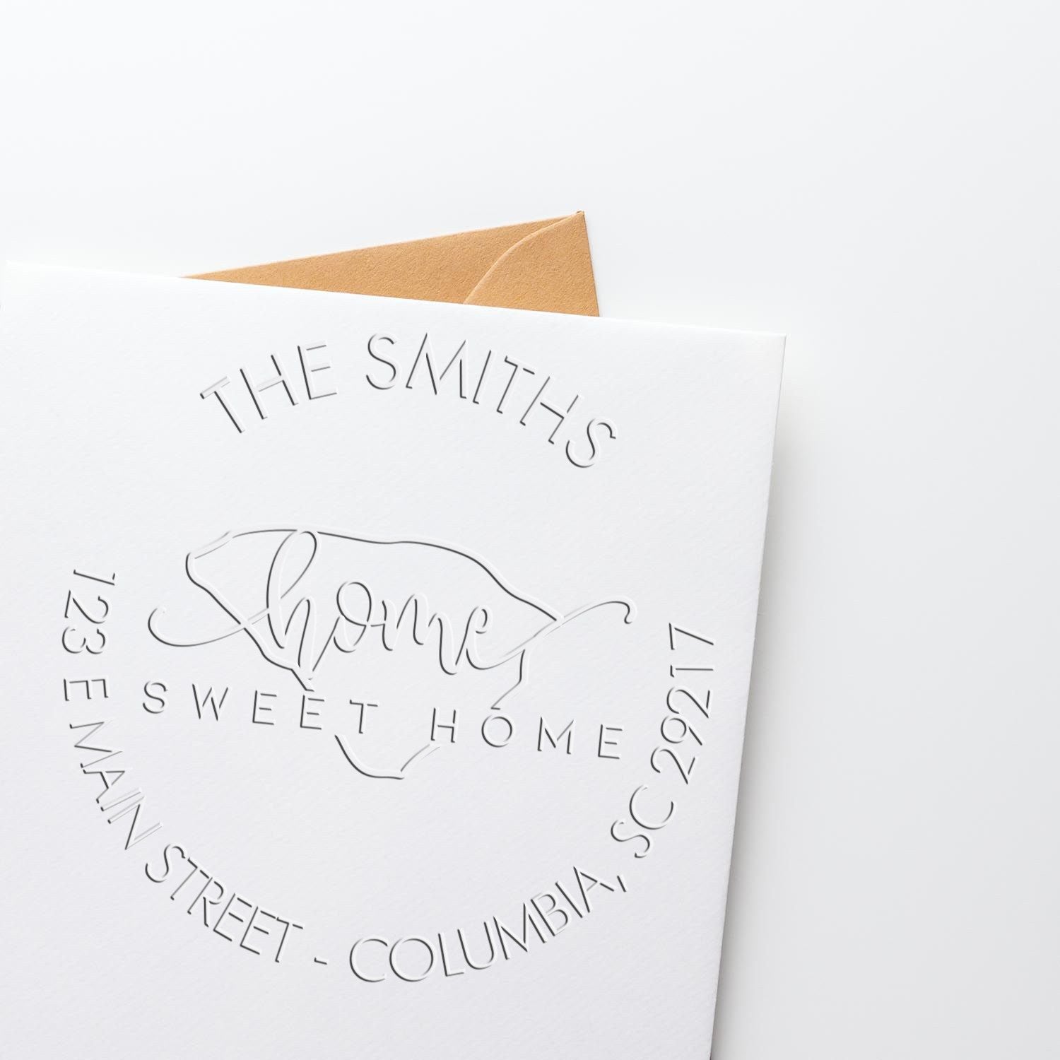 White embossed custom seal card reading The Smiths Home Sweet Home, with tan envelope behind.