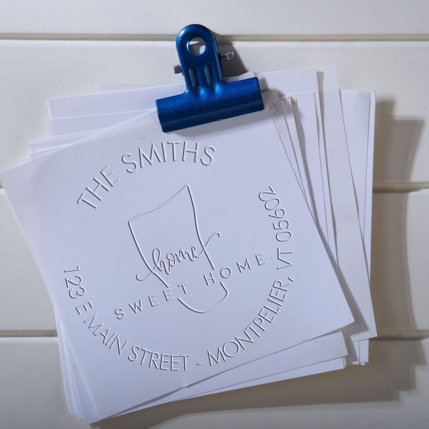 Blue binder clip holding white embossed custom stamp and seal sheets for The Smiths, Sweet Home address design.