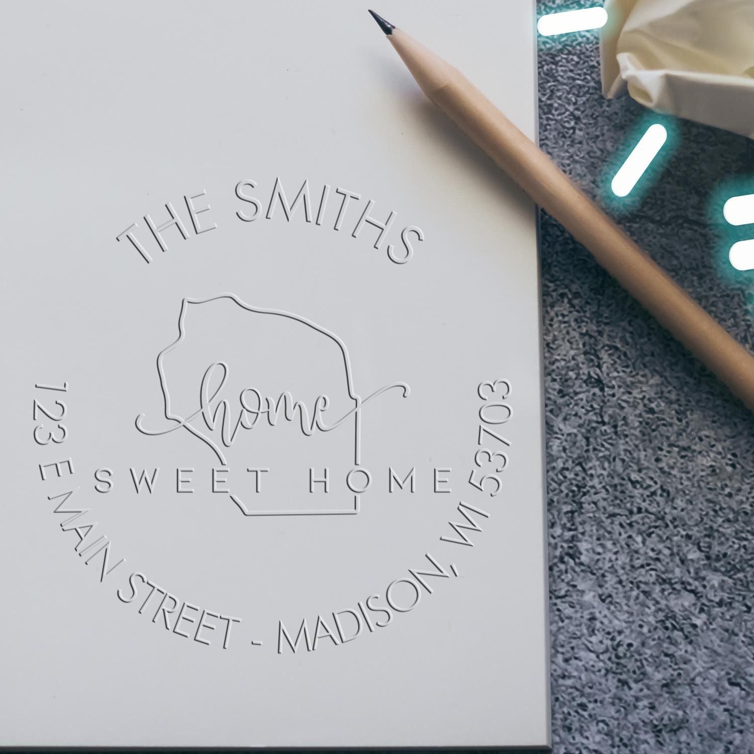 White embossed custom stamp and seal for The Smiths Sweet Home, with pencil on gray textured background.