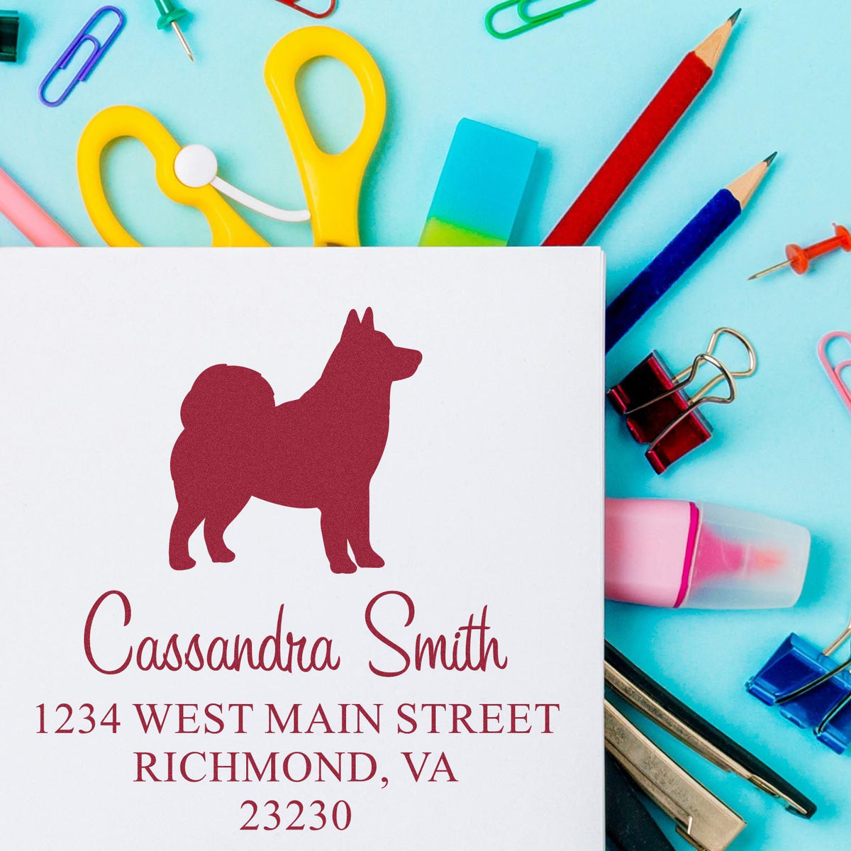 Custom stamp and seal with burgundy dog silhouette, name and address, on a blue desk with colorful stationery.