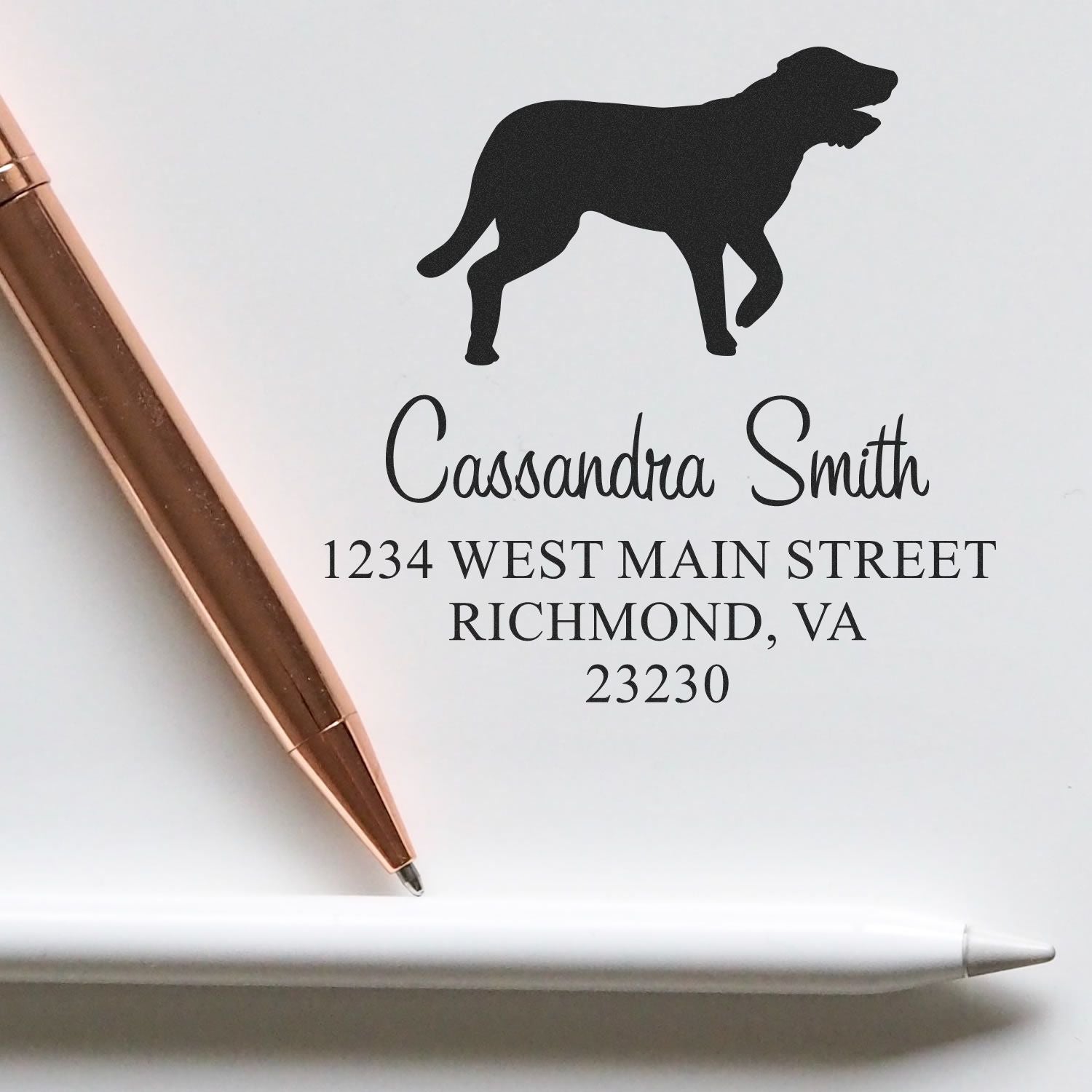 Custom black dog stamp and seal with Cassandra Smith return address in black on white paper, beside a rose gold pen.