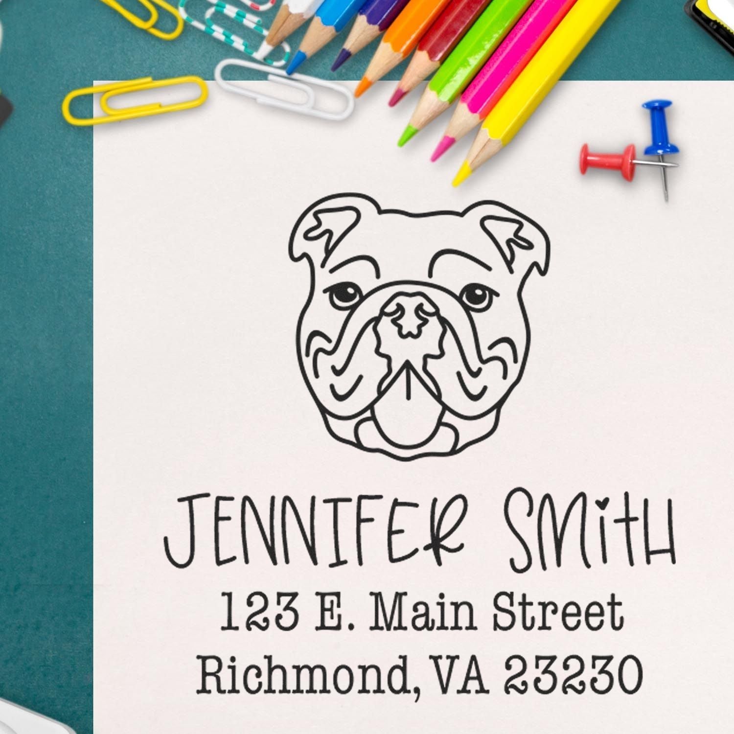 Custom bulldog address stamp and seal on white paper, with black text, colorful pencils, paper clips, and push pins on teal.