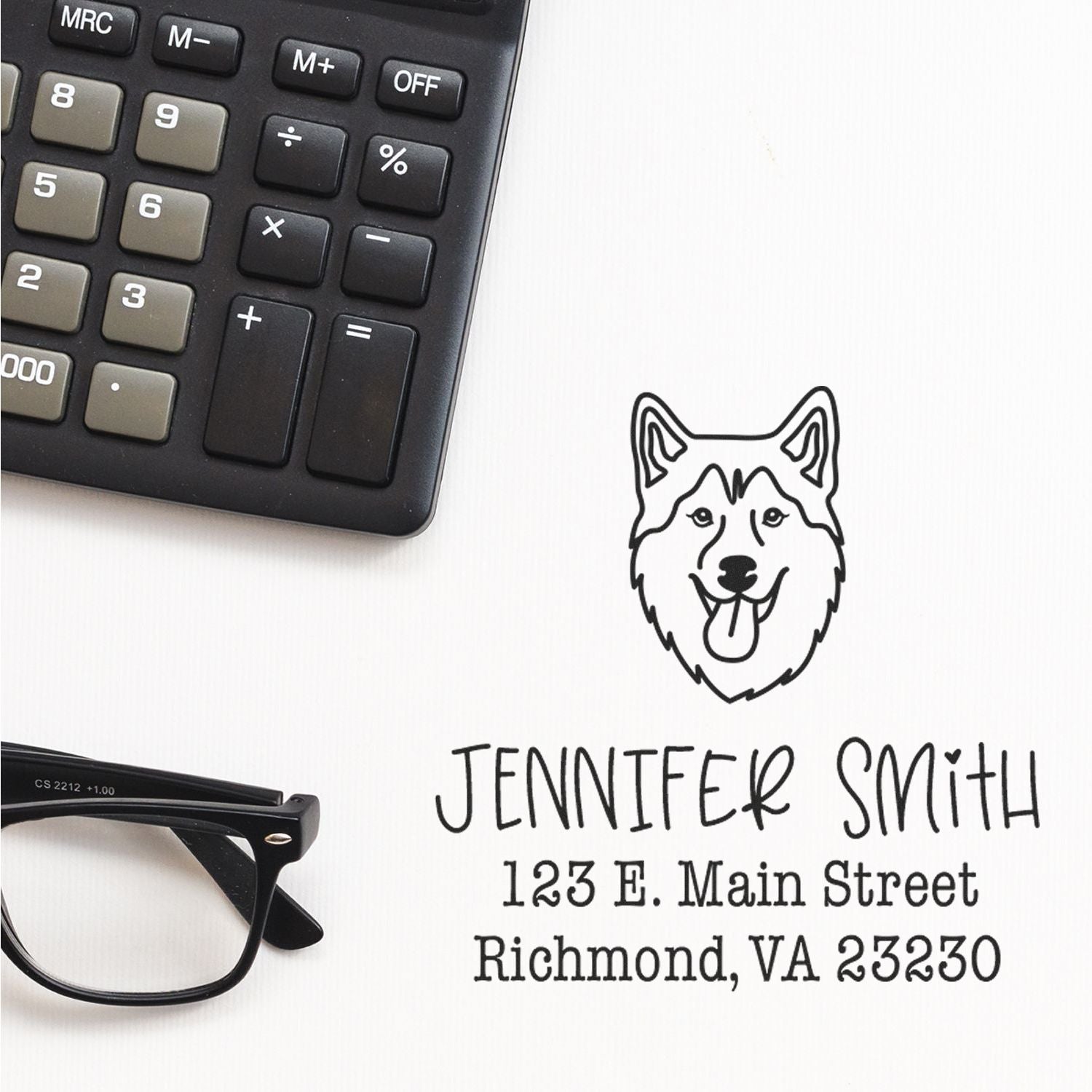 Black custom stamp seal with husky logo, Jennifer Smith name and address beside calculator and eyeglasses on white background.