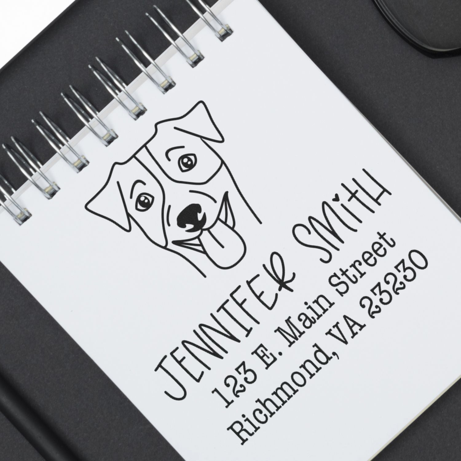 Custom rubber stamp and address seal in black on white spiral notebook, featuring a line-art dog and Jennifer Smith address.