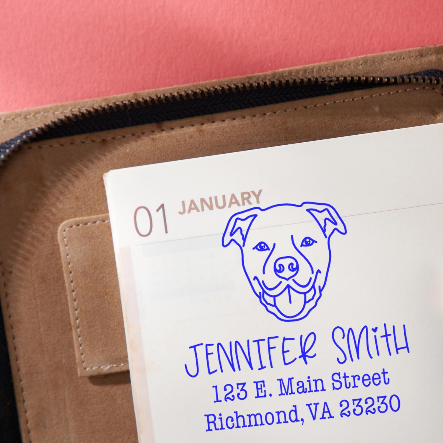 Blue custom address stamp with dog seal on a white planner page dated January 1, beside a tan leather case.