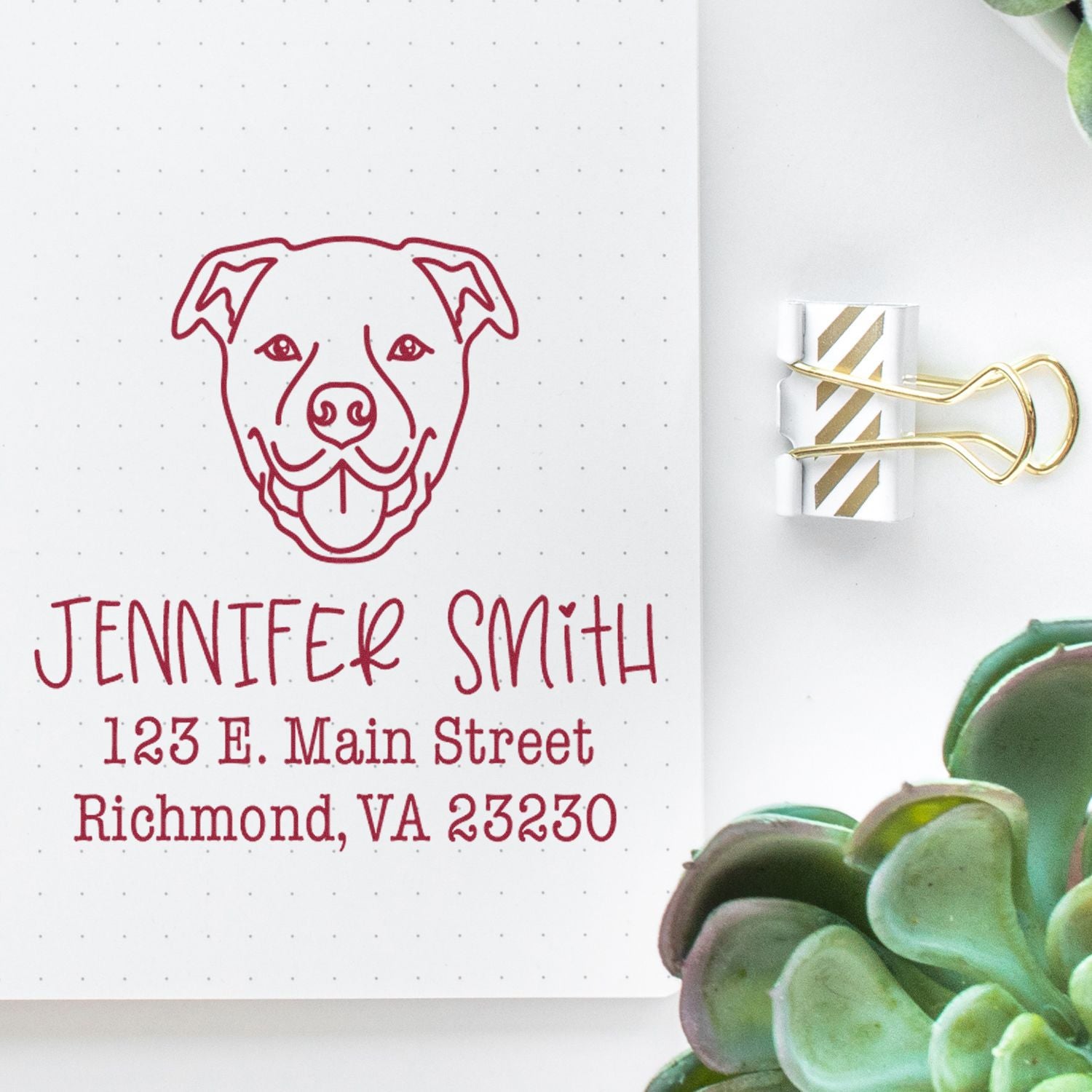 Custom burgundy dog logo stamp and address seal on white dotted paper, clipped with a gold binder clip beside green succulent.