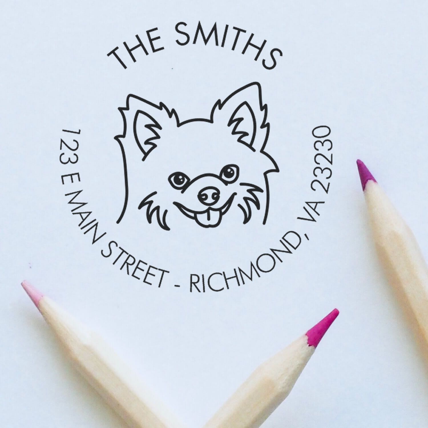 Custom black round address stamp and seal for The Smiths with dog logo, on white paper, framed by pink-tipped pencils.