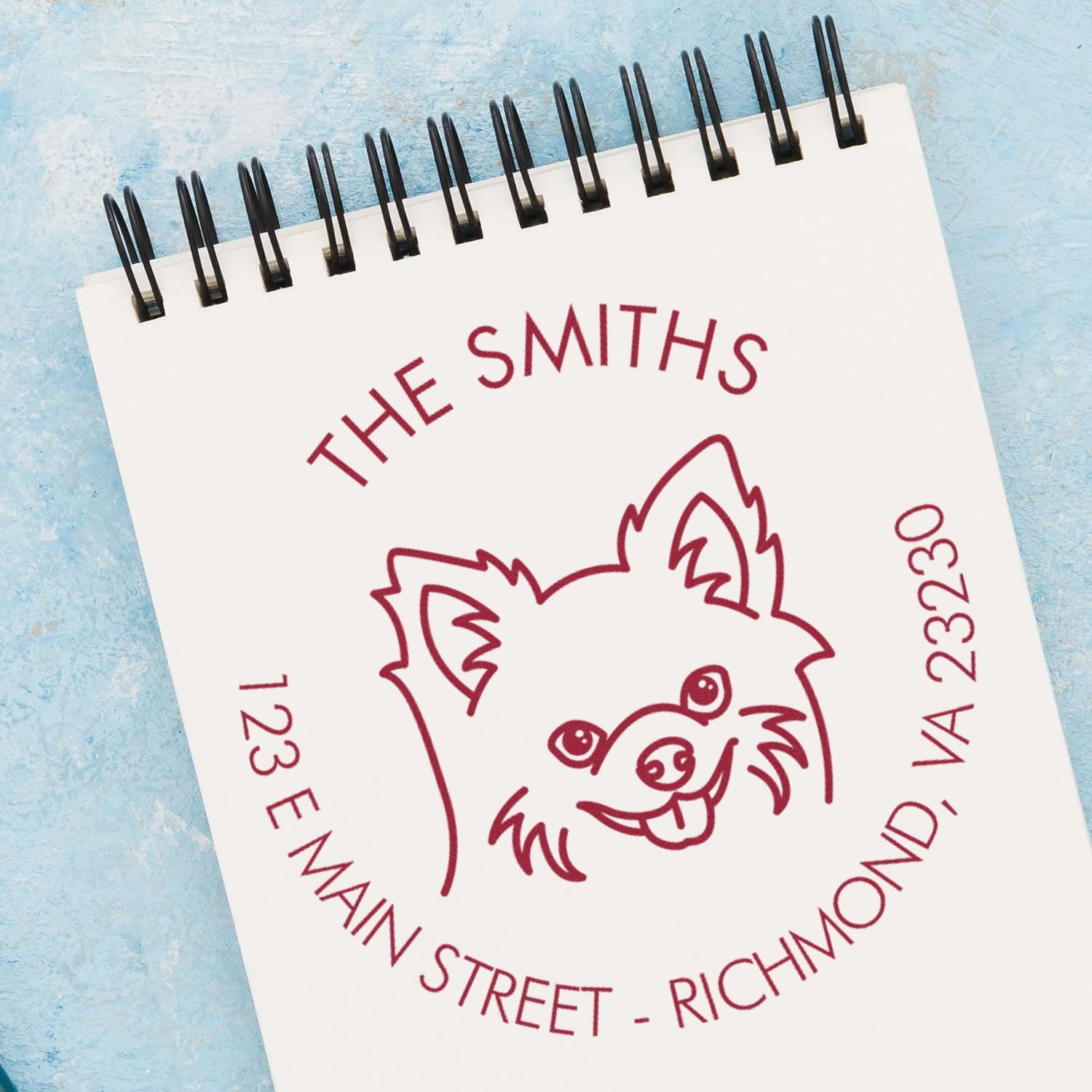 Burgundy custom address stamp and seal with dog logo for The Smiths, 123 E Main St, Richmond, VA 23230 on white notebook.