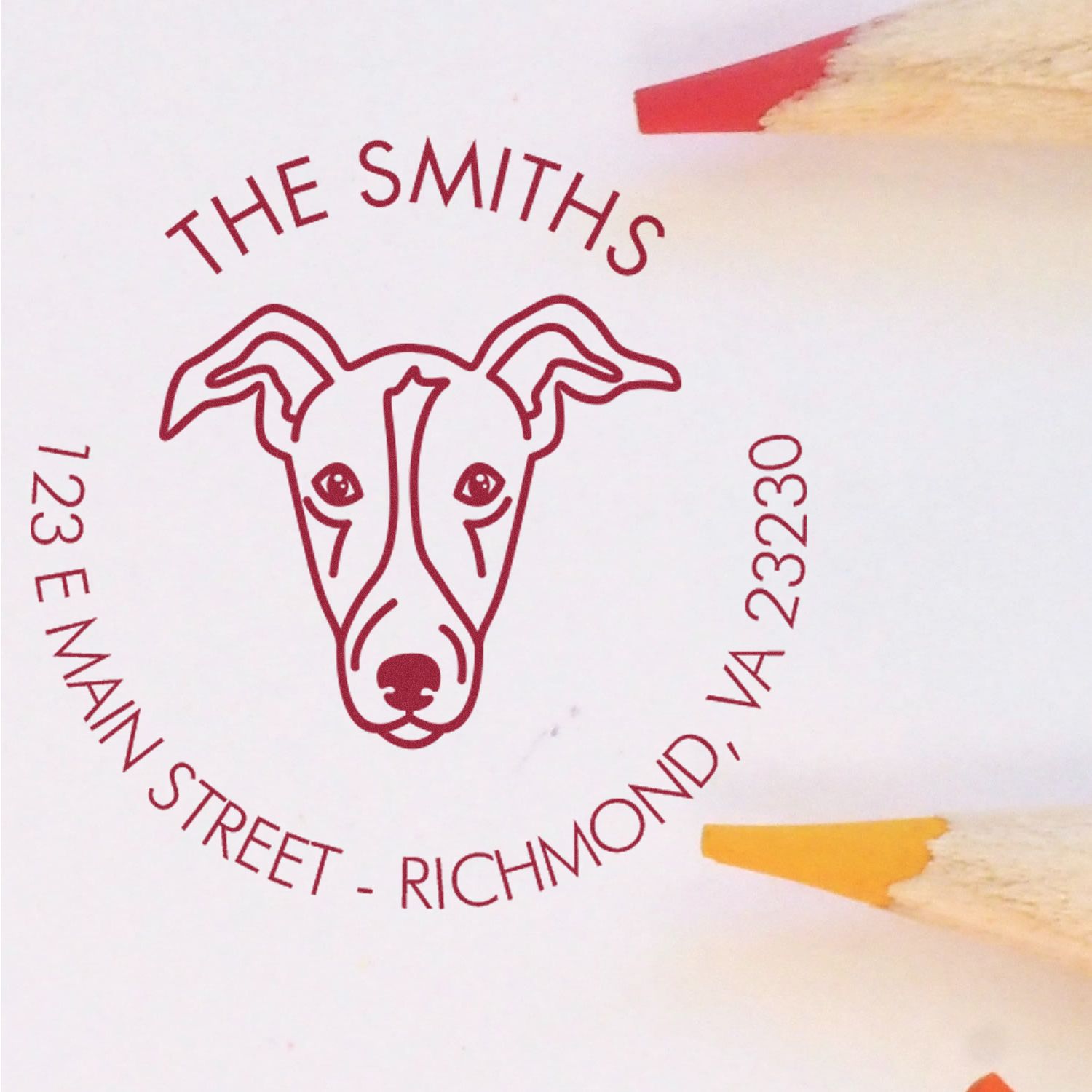 Maroon custom stamp seal with dog logo, The Smiths, 123 E Main Street, Richmond, VA 23230, on white paper with red and yellow pencils.