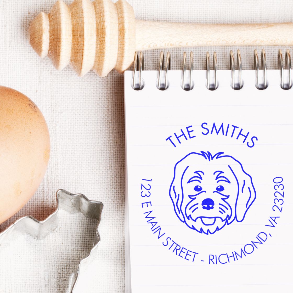 Blue custom dog address stamp and seal on notebook, with wooden handle and clear seal ring on beige fabric.