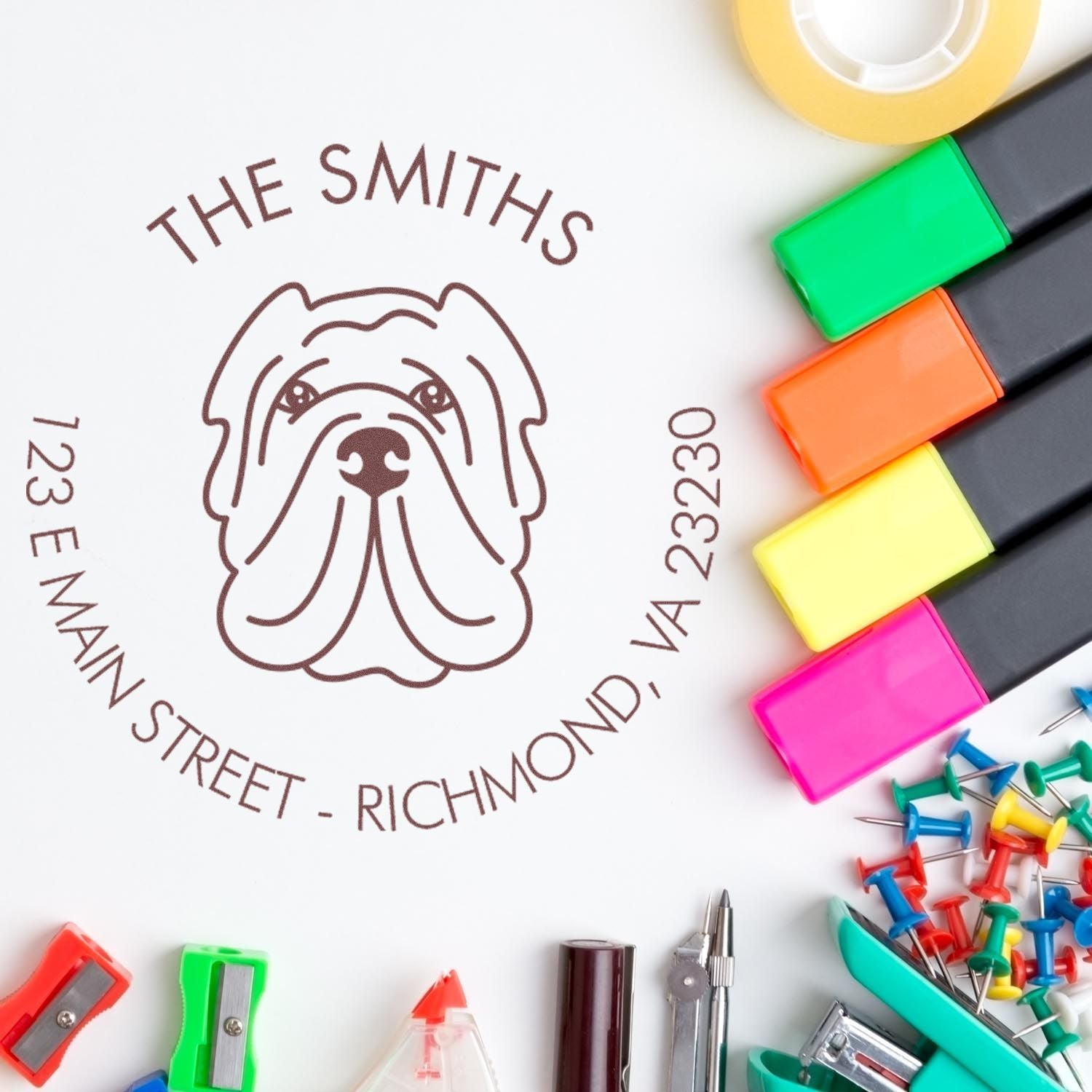 Custom dog logo address stamp with brown text, surrounded by colorful stamp and seal markers, pins and office tools on white.