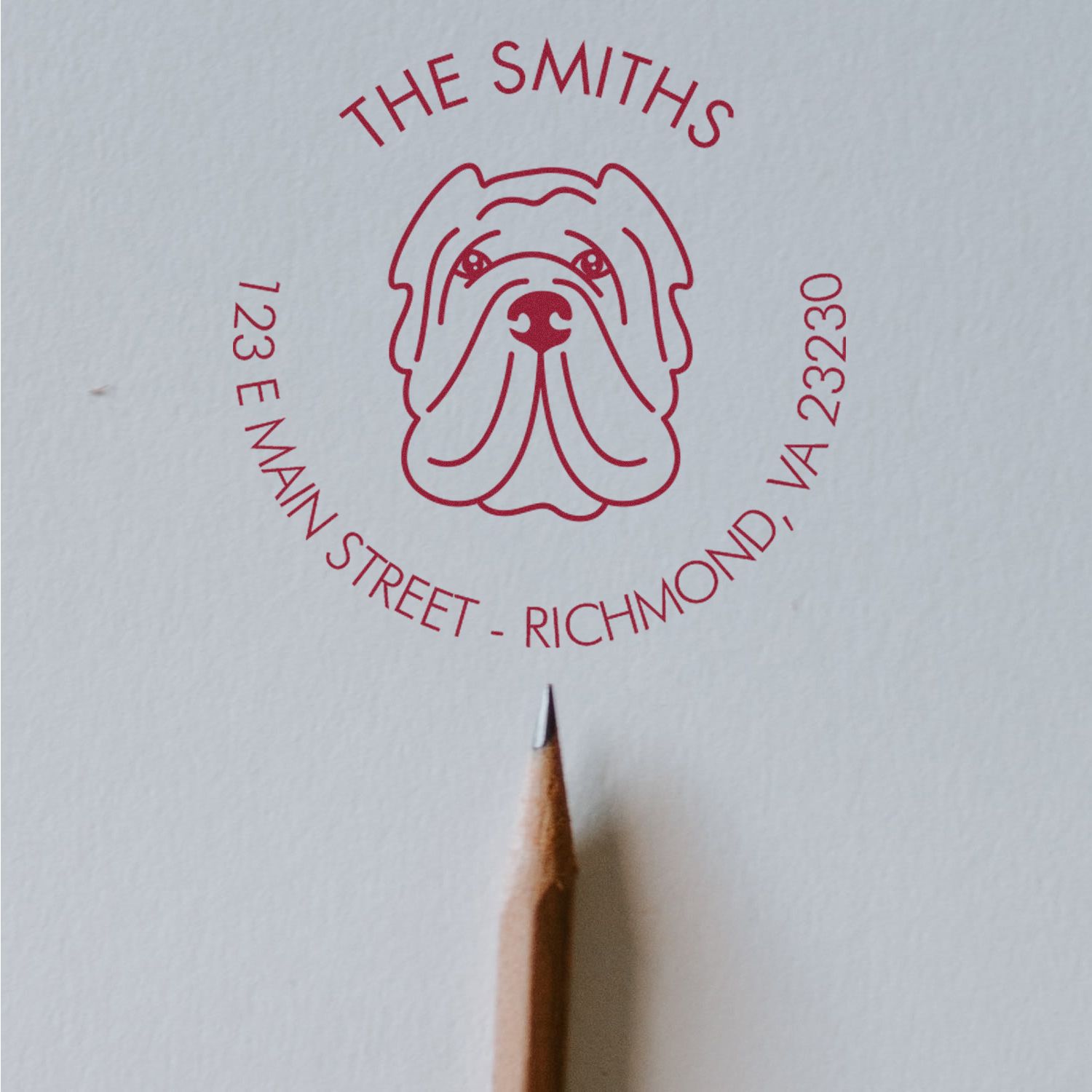 Red bulldog address stamp seal for The Smiths, 123 E Main Street, Richmond, VA 23230, on white paper with pencil tip.