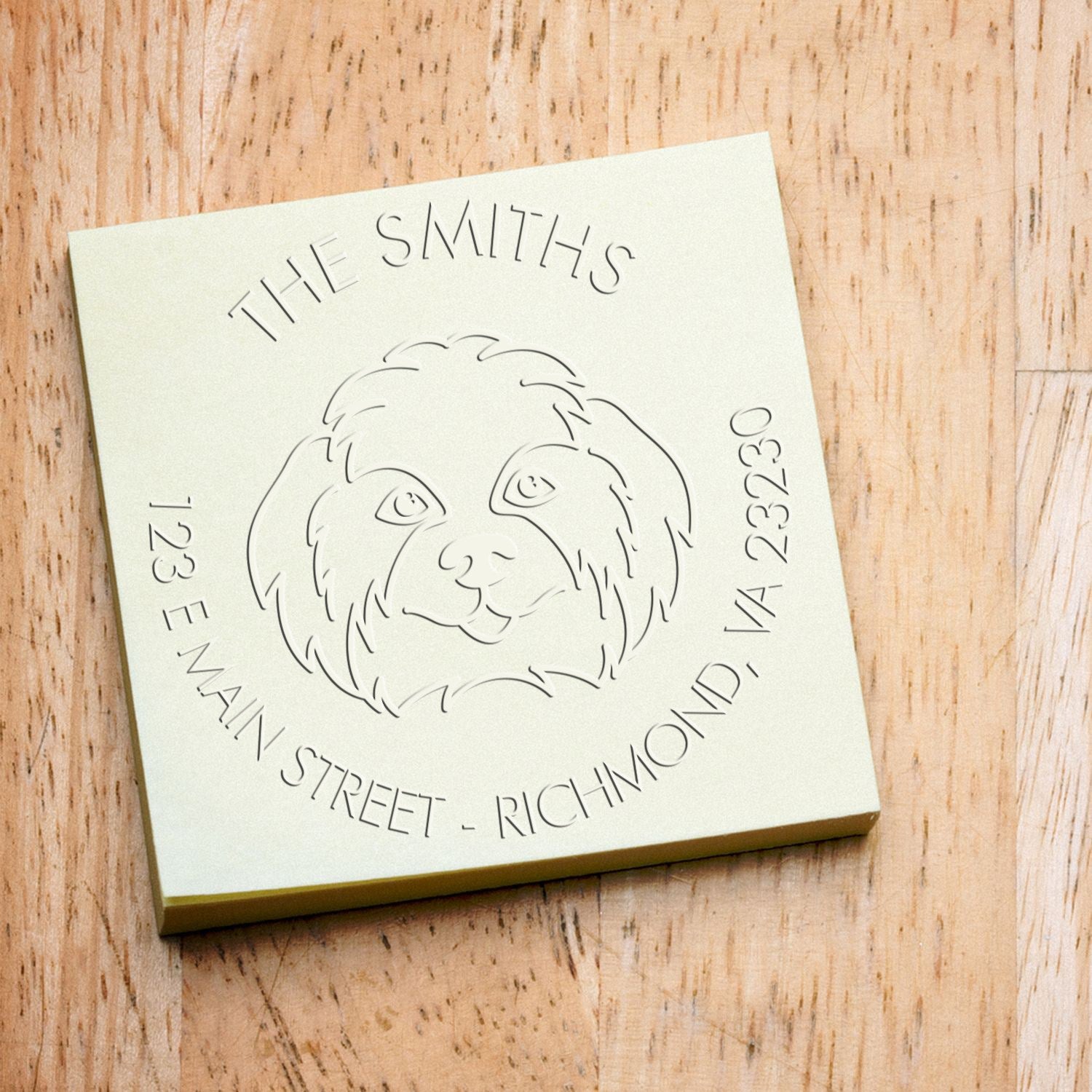 Cream square custom stamp and seal with engraved dog face and text on a light wood background.