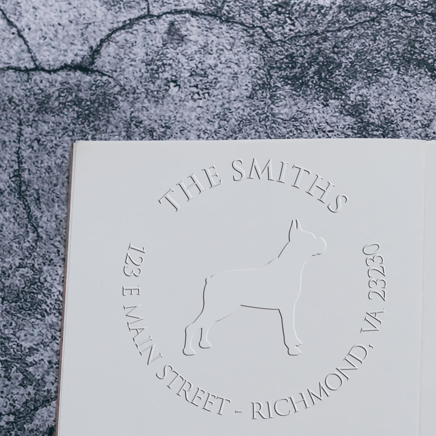 White embossed stamp seal for The Smiths, with dog outline and address, on a gray textured background.