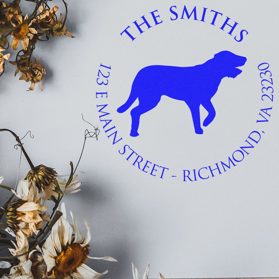 Blue custom dog stamp seal reading The Smiths with Richmond, VA address on white background, framed by dried flowers.